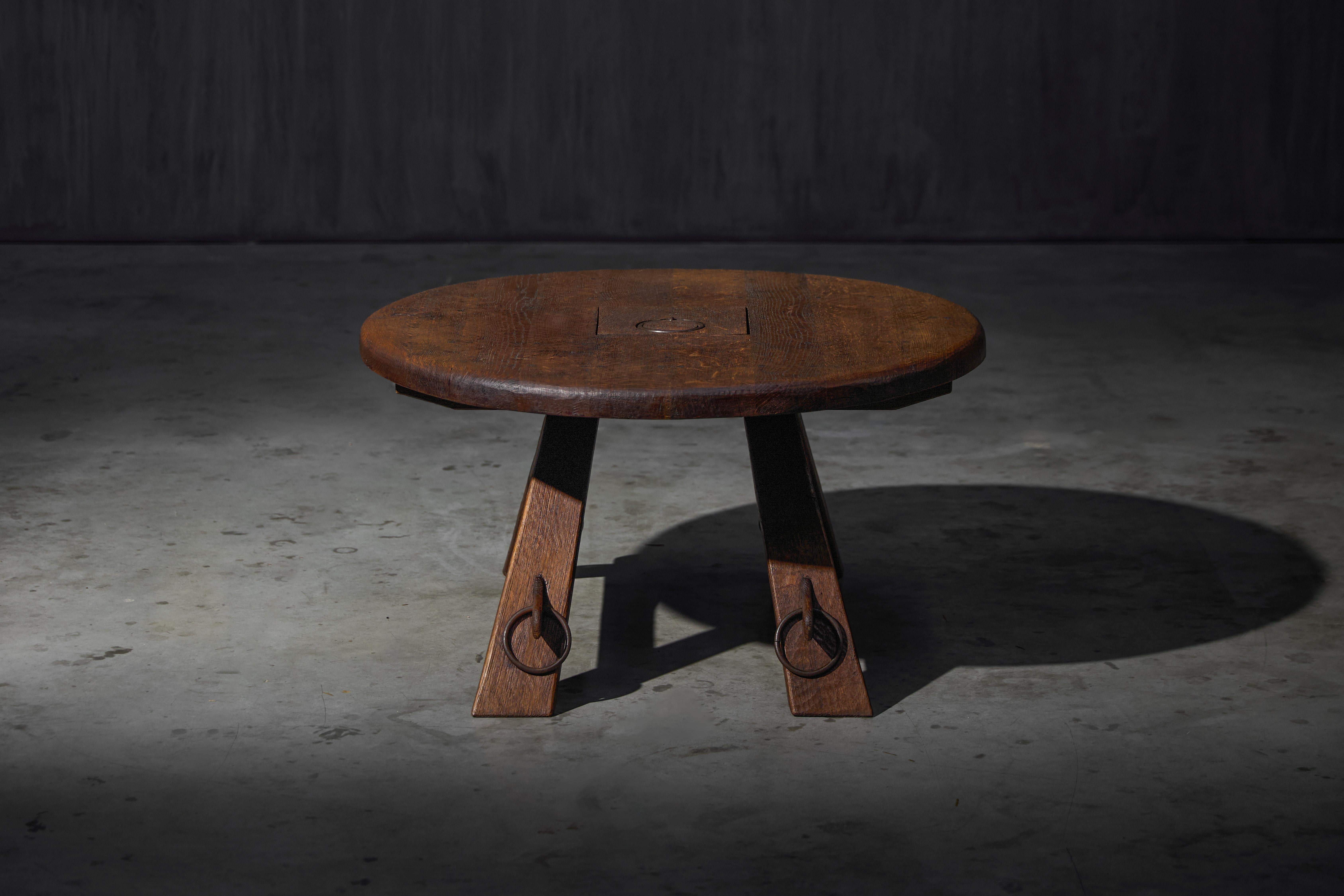 Esta mesa de centro redonda presenta una superficie de roble desgastada por el tiempo, rica en carácter y pátina, que refleja años de uso. El detalle del anillo central sugiere una herencia utilitaria, añadiendo autenticidad rústica. 
