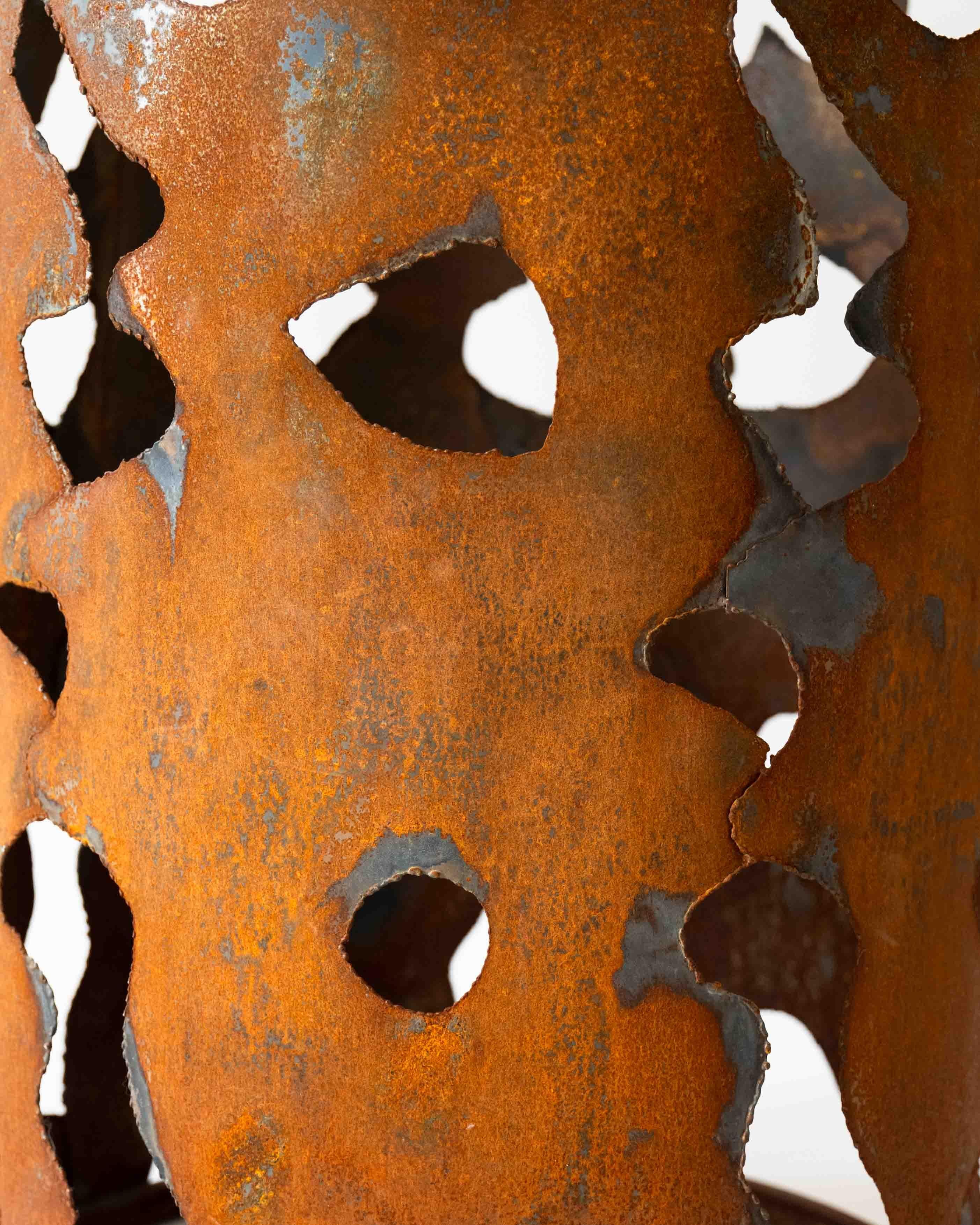 Questo tavolino scultoreo è caratterizzato da uno zoccolo cilindrico in acciaio con un'espressiva silhouette tagliata a mano. La patina ossidata ne esalta la consistenza grezza e organica, evocando l'aspra bellezza del metallo rovinato dalle