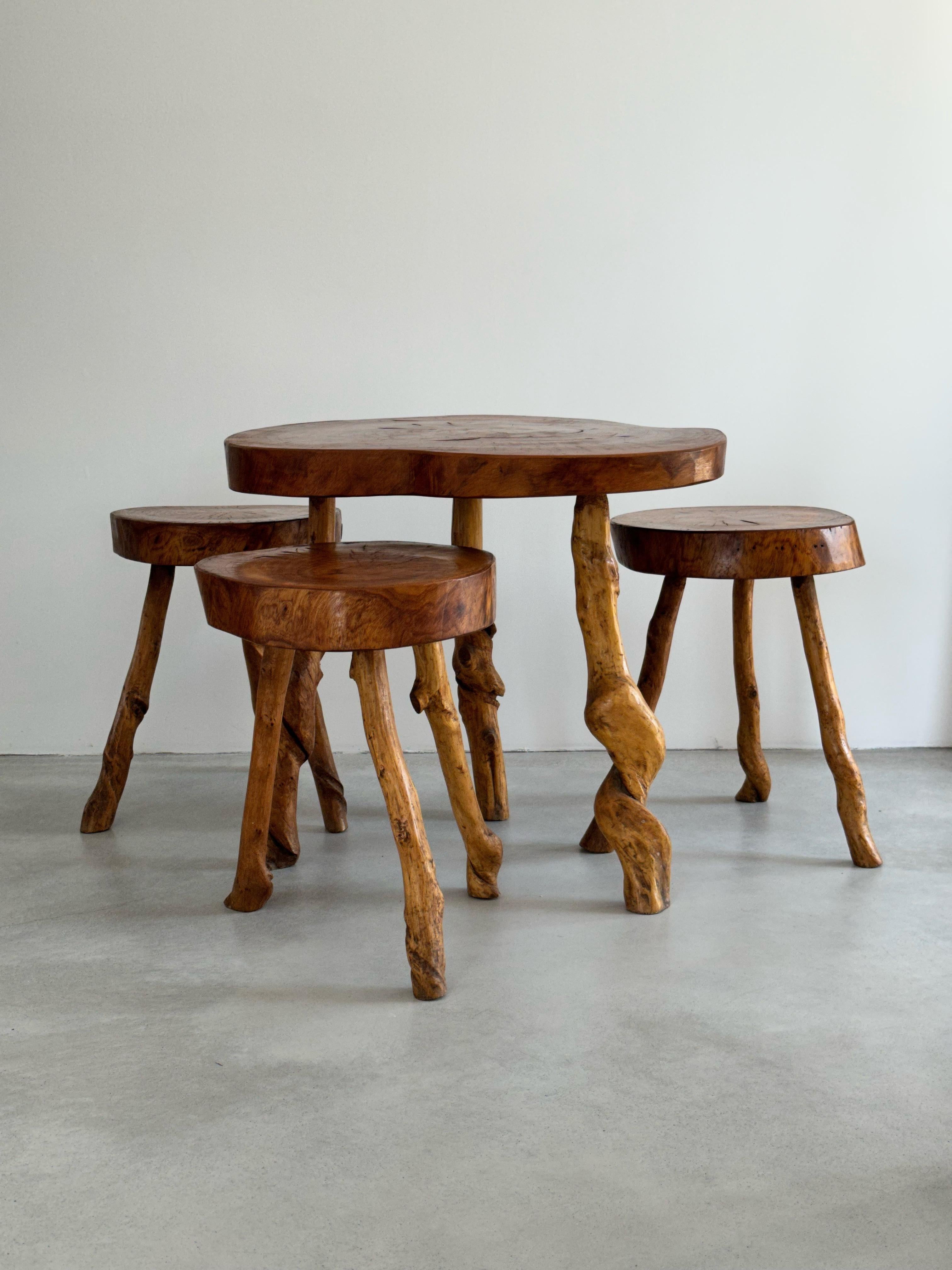 This primitive set was produced by a French craftsman in the 1960s. 
The stools all have a slightly different shape, the table is of the same construction, which gives them their rustic and naturalistic appearance. 
The stools and the table have