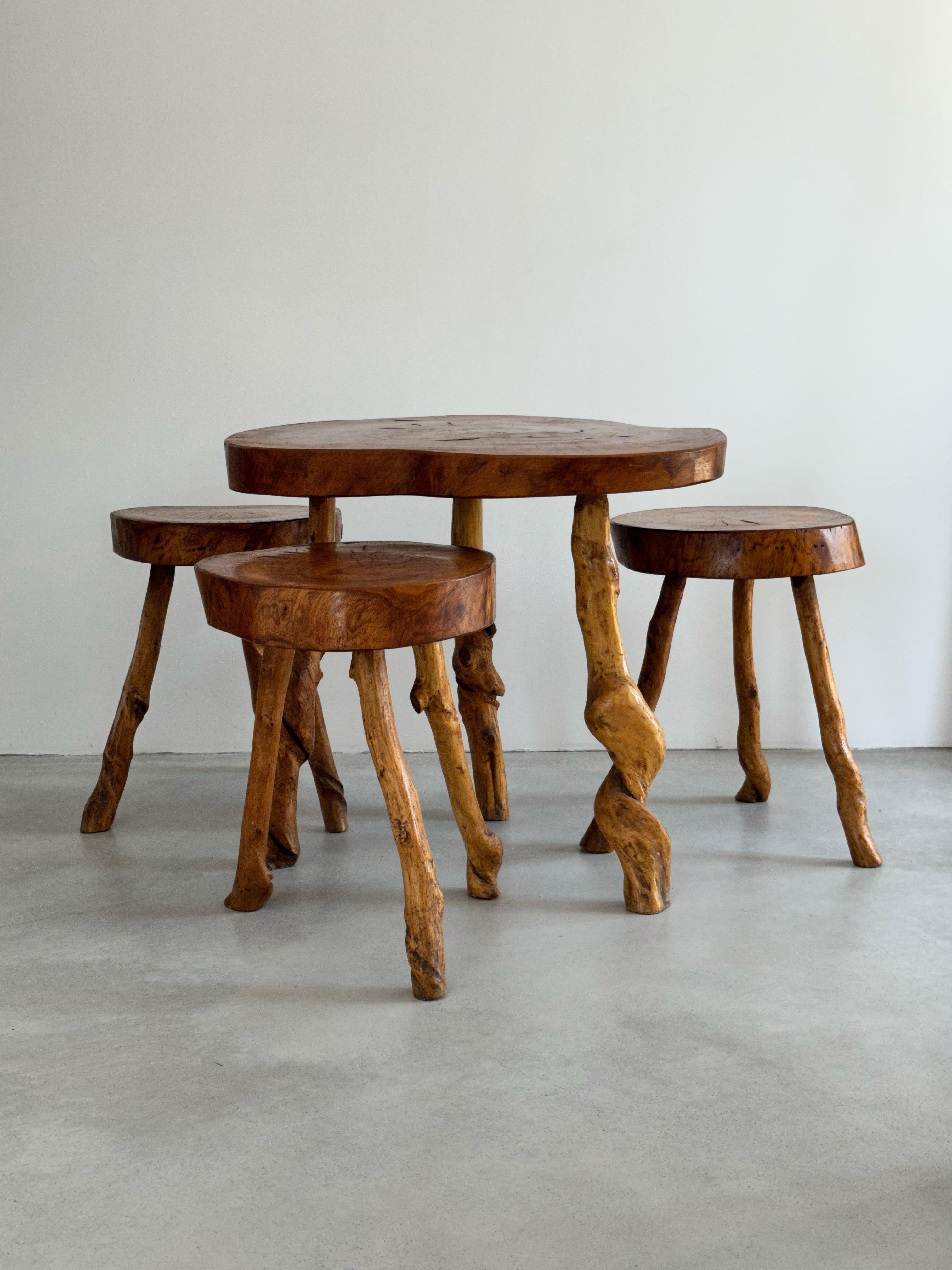 Cet ensemble primitif a été fabriqué par un artisan français dans les années 1960. 
Les tabourets ont tous une forme légèrement différente, la table est de la même construction, ce qui leur donne leur aspect rustique et naturaliste. 
Les tabourets