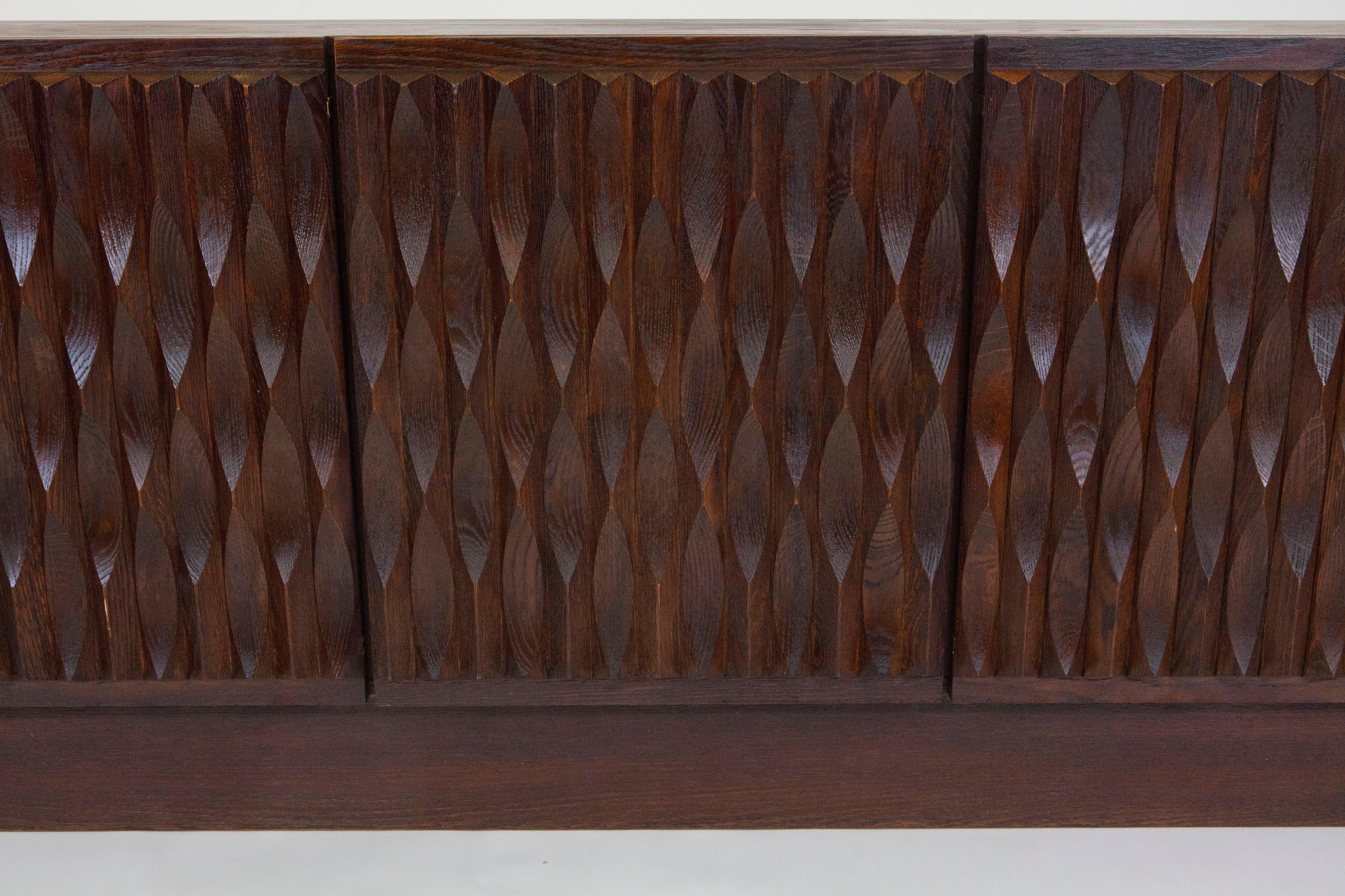 A dark brown vintage Belgian brutalist sideboard with graphic wave detail on the front five doors. The interior has one set of drawers with other openings having shelves.