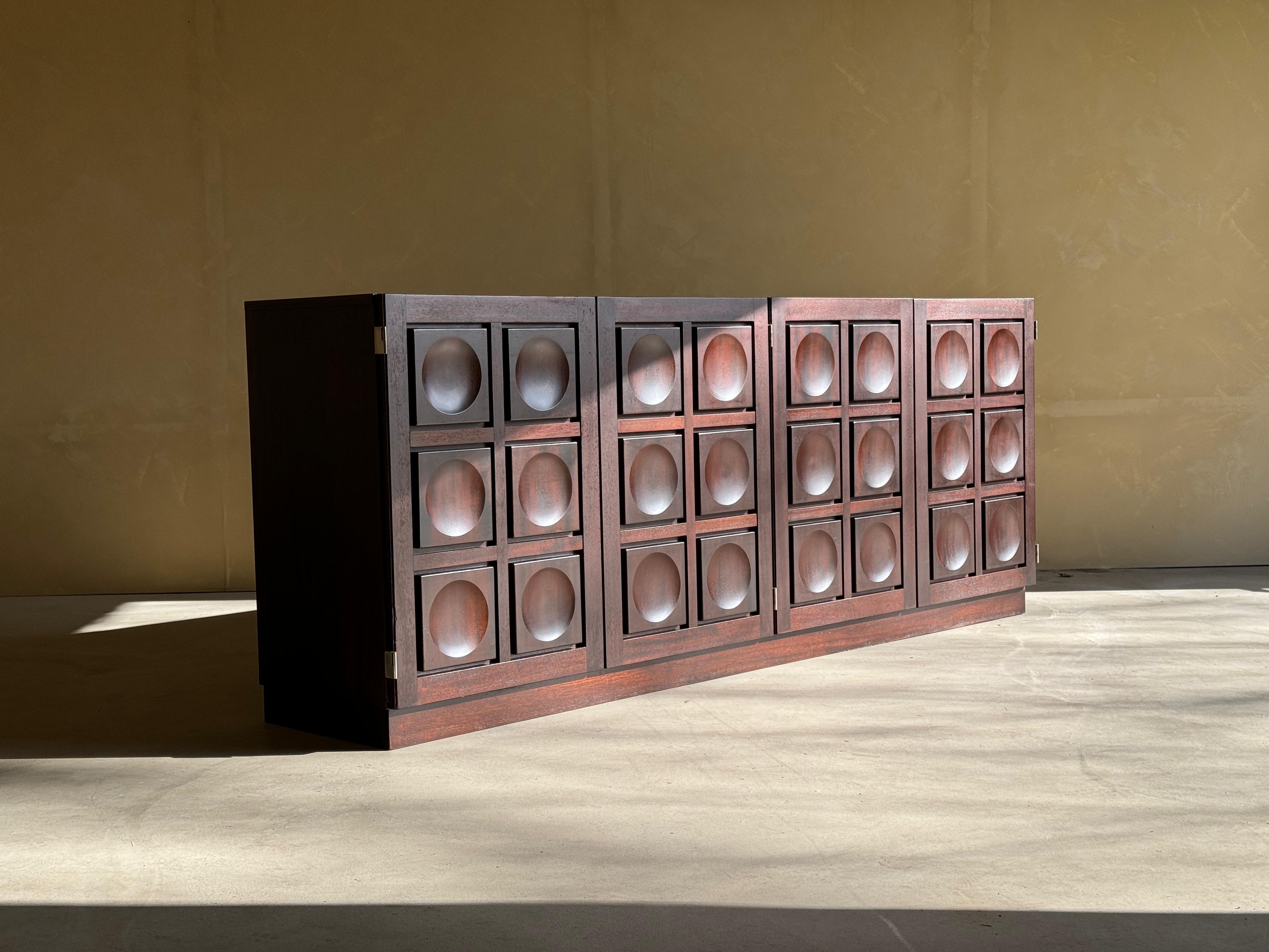 Sideboard or credenza in burgundy colored oak, Belgium, 1970s.

This very evocative cabinet features a clear rhythm and flow established by means of a well-thought-out lay out that is utterly well-balanced. The carved circles immediately catch the