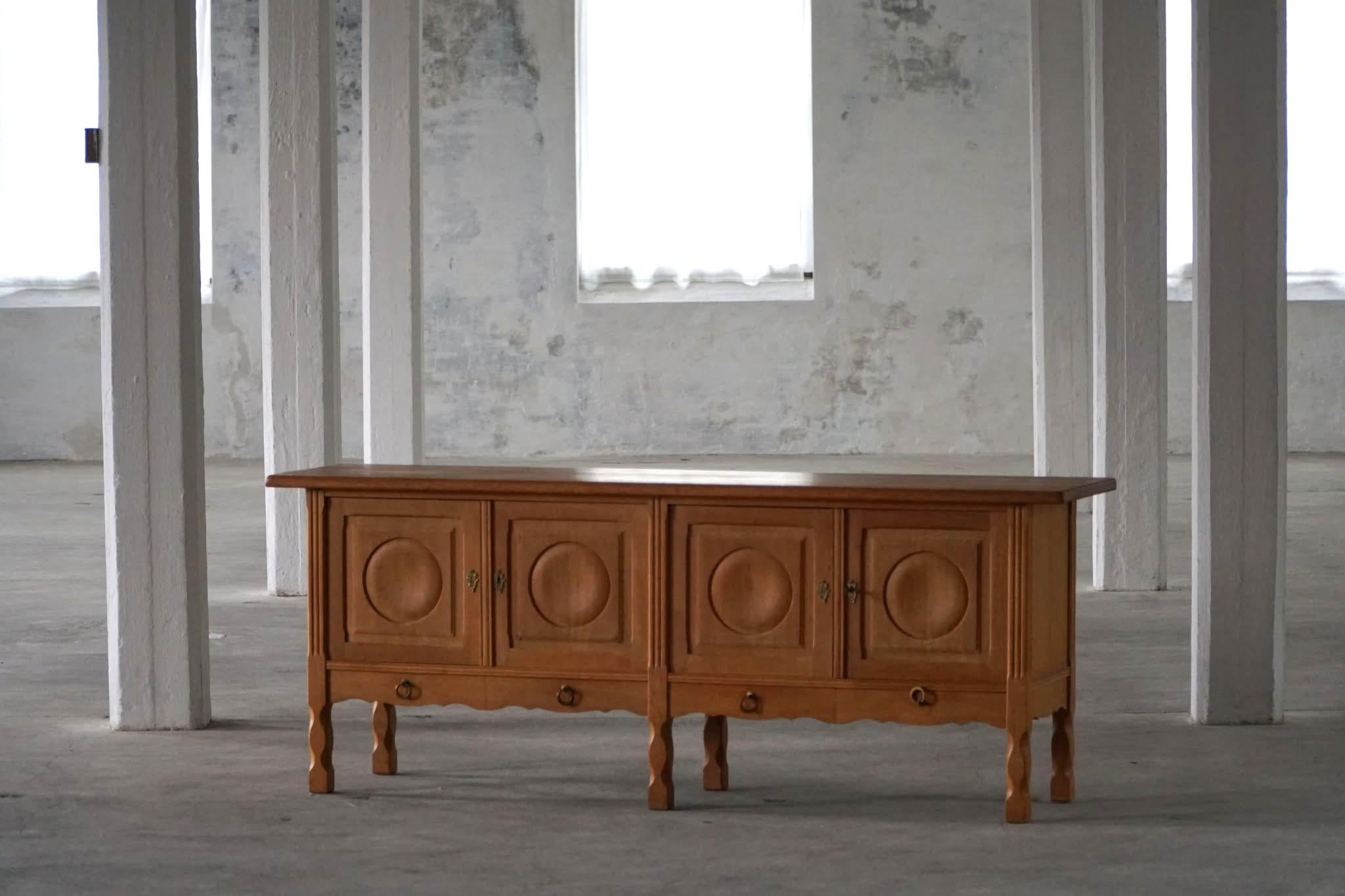 A fantastic low classic sideboard in solid oak. Made by a Danish Cabinetmaker, Anker Sørensen in the 1960s. The piece is made in solid oak with four paneled doors adorned with bold circular relief carvings. The brass hardware adds a refined touch