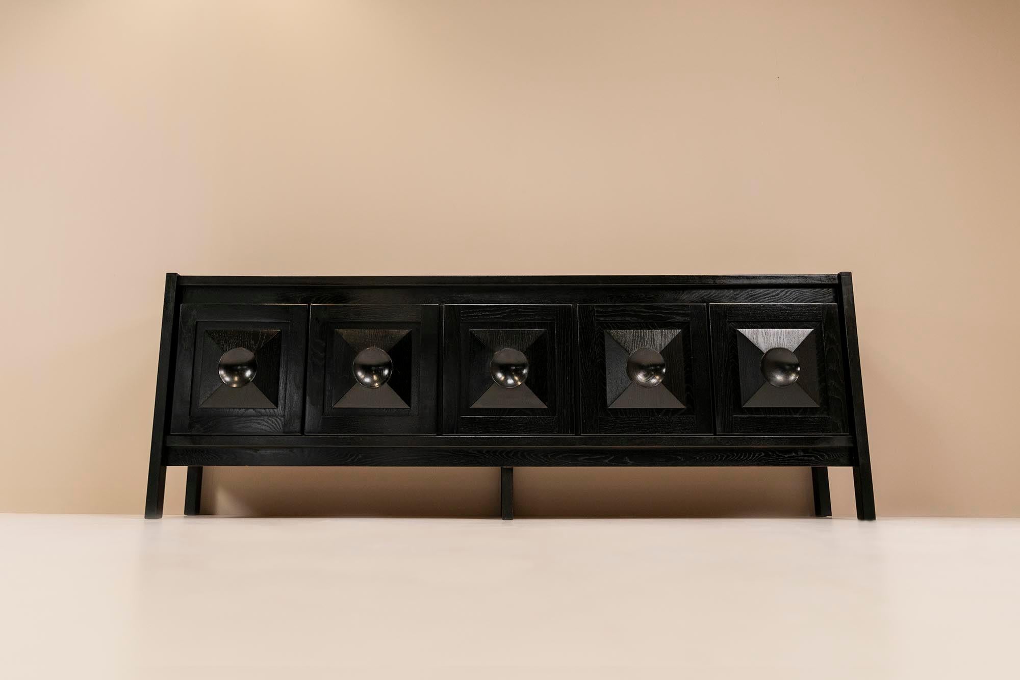 A beautiful brutalist sideboard in the style of De Coene from the 1970s. This item is made of black-stained solid oak and has five doors. These doors have a nice thickness and carry a three-dimensional pattern on the front. They open and close