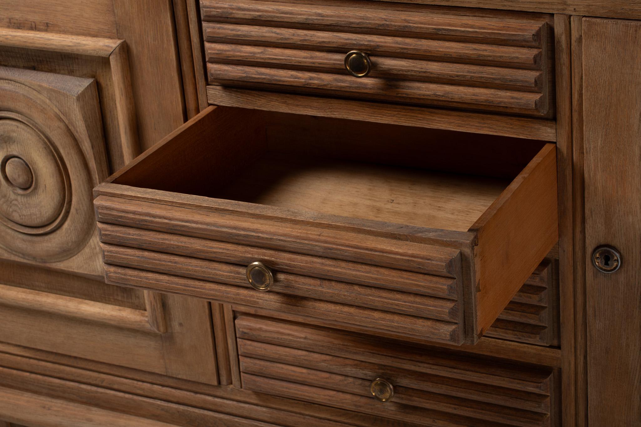 This sculptural sideboard holds a quiet monumentality—its façade a study in balance, depth, and geometric relief. Two symmetrical doors are adorned with deeply carved concentric medallions, each centered within a bevel-edged square that projects