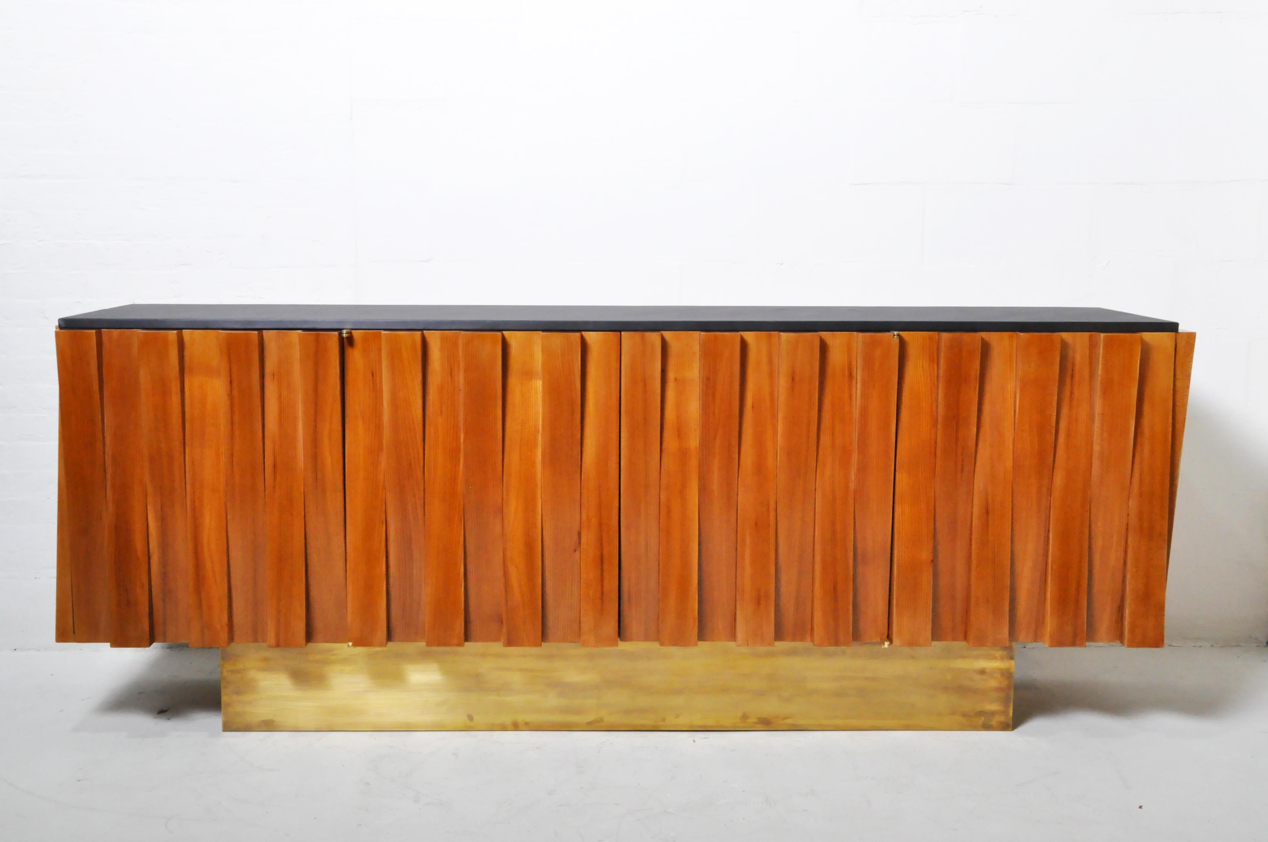This impressive Mid-Century Modern (or Brutalist sideboard) is made from straight-grained light walnut veneers applied to alternating raised dentils. The four doors feature brass scissor hinges and are without metal handles. The interior, also