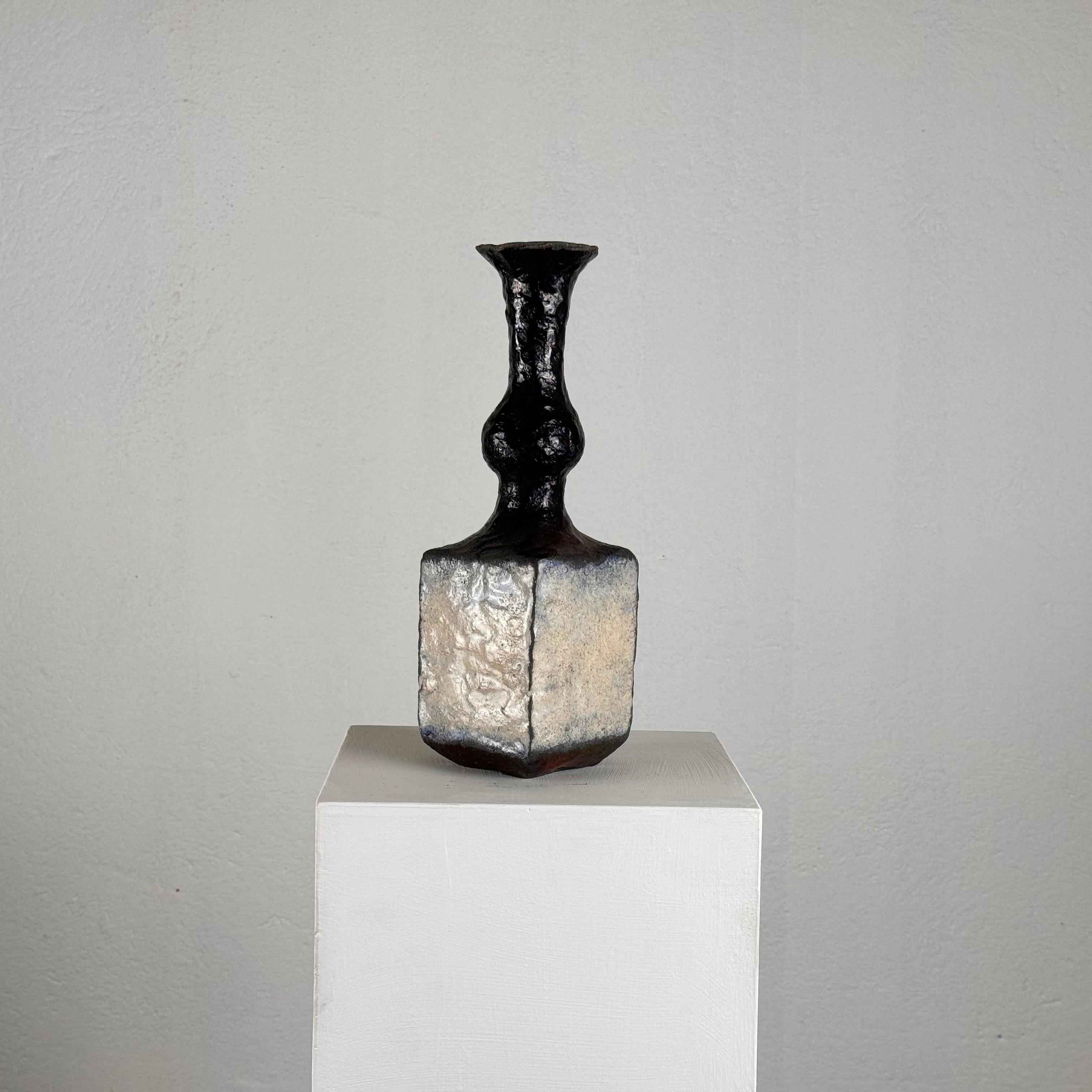 This stunning brutalist single-stem vase, crafted from raku ceramic in the 1970s, is a highly decorative piece that embodies the raw and artistic essence of the brutalist movement. The vase features a unique, textured surface with the characteristic