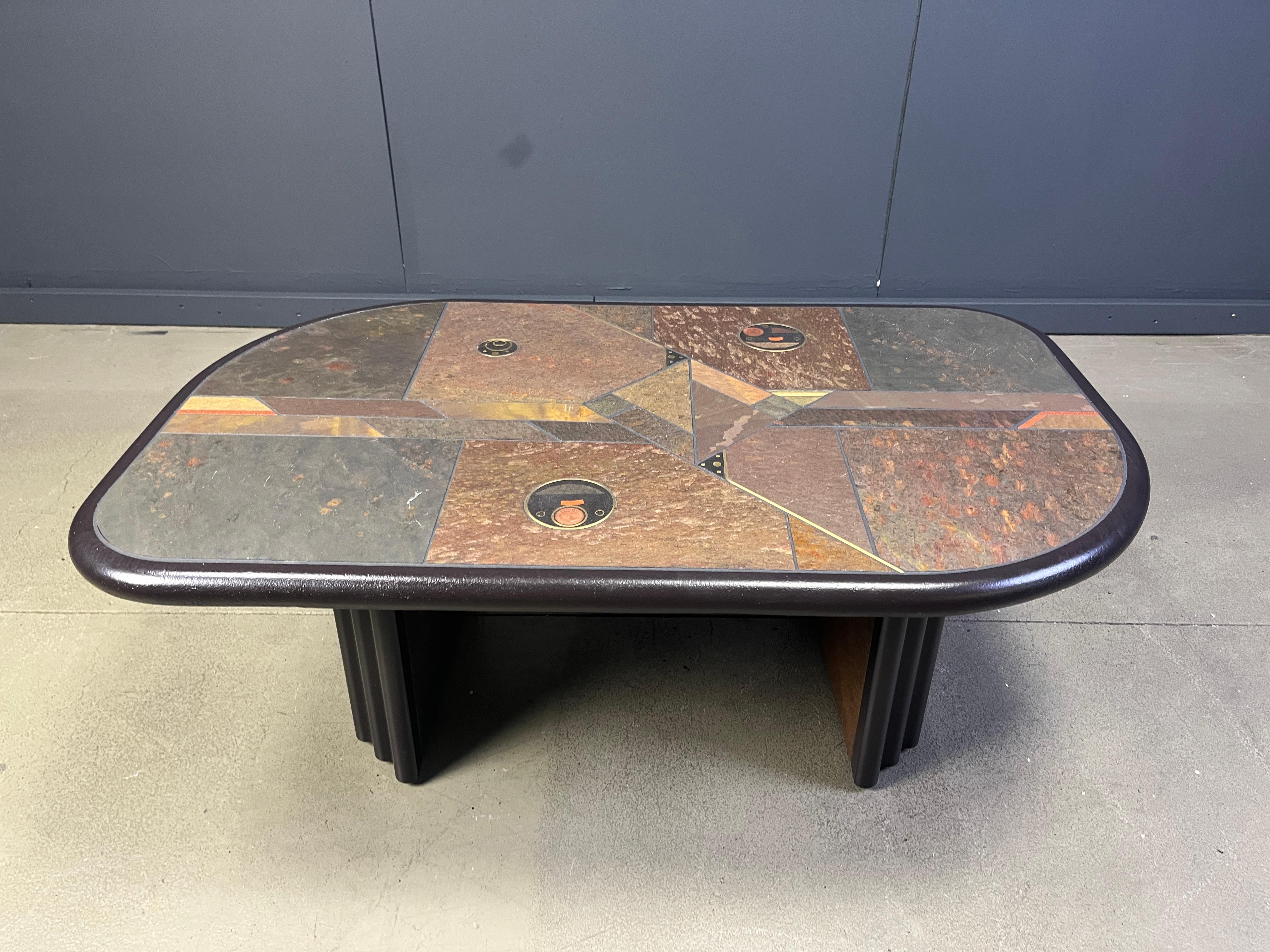 Table basse brutaliste à plateau en ardoise et pierre naturelle avec incrustation de cuivre et de laiton.

Base en bois noir.

Le tableau est signé, mais on ne voit pas par qui.

Bon état.

Très proche du style de Paul Kingma.

Années 1980 -