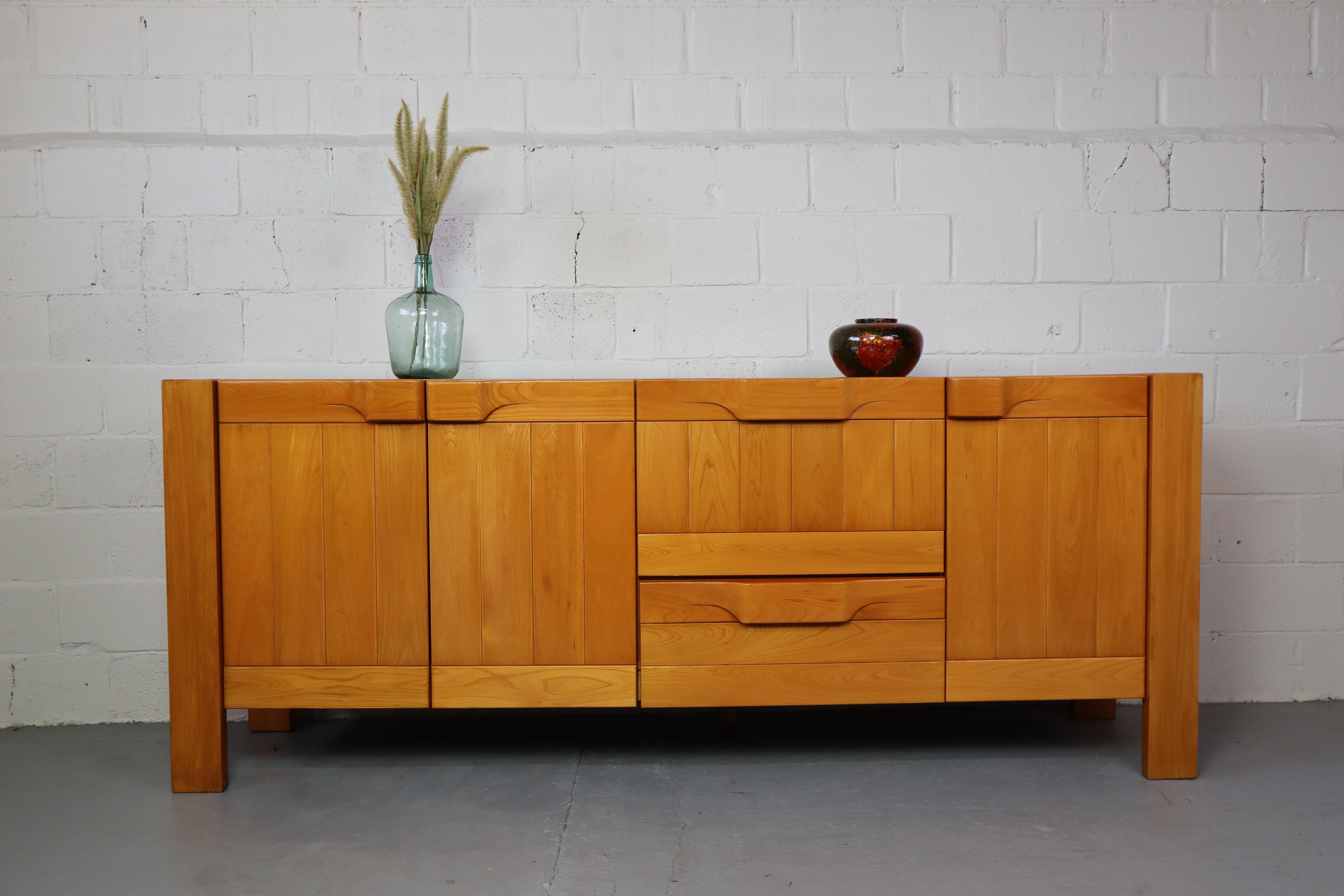 Brutalist solid Elm sideboard by Maison Regain, France.  The large curved handles which have been carved from a single piece of solid wood  are very typical for Maison Regains designs.
The cabinet has one drawer and a flap door above it. The