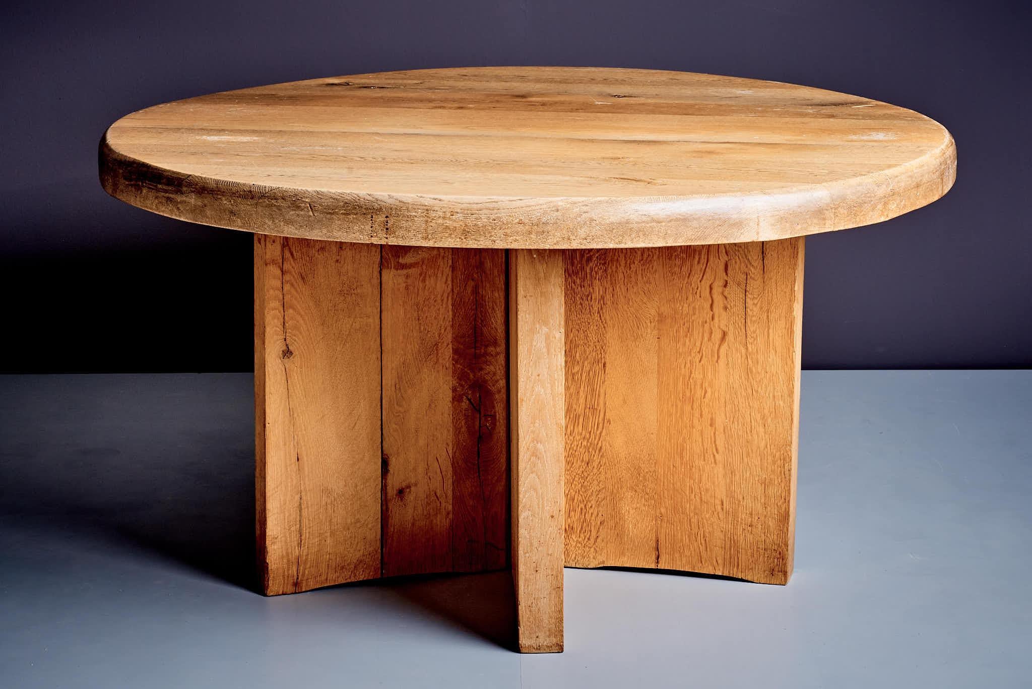 Crafted from solid oak, this table showcases natural grain and knots, exuding rustic charm. Its 70mm thick, round tabletop features a hand-finished surface, supported by a sturdy, geometric base of five interlocking panels. It blends timeless
