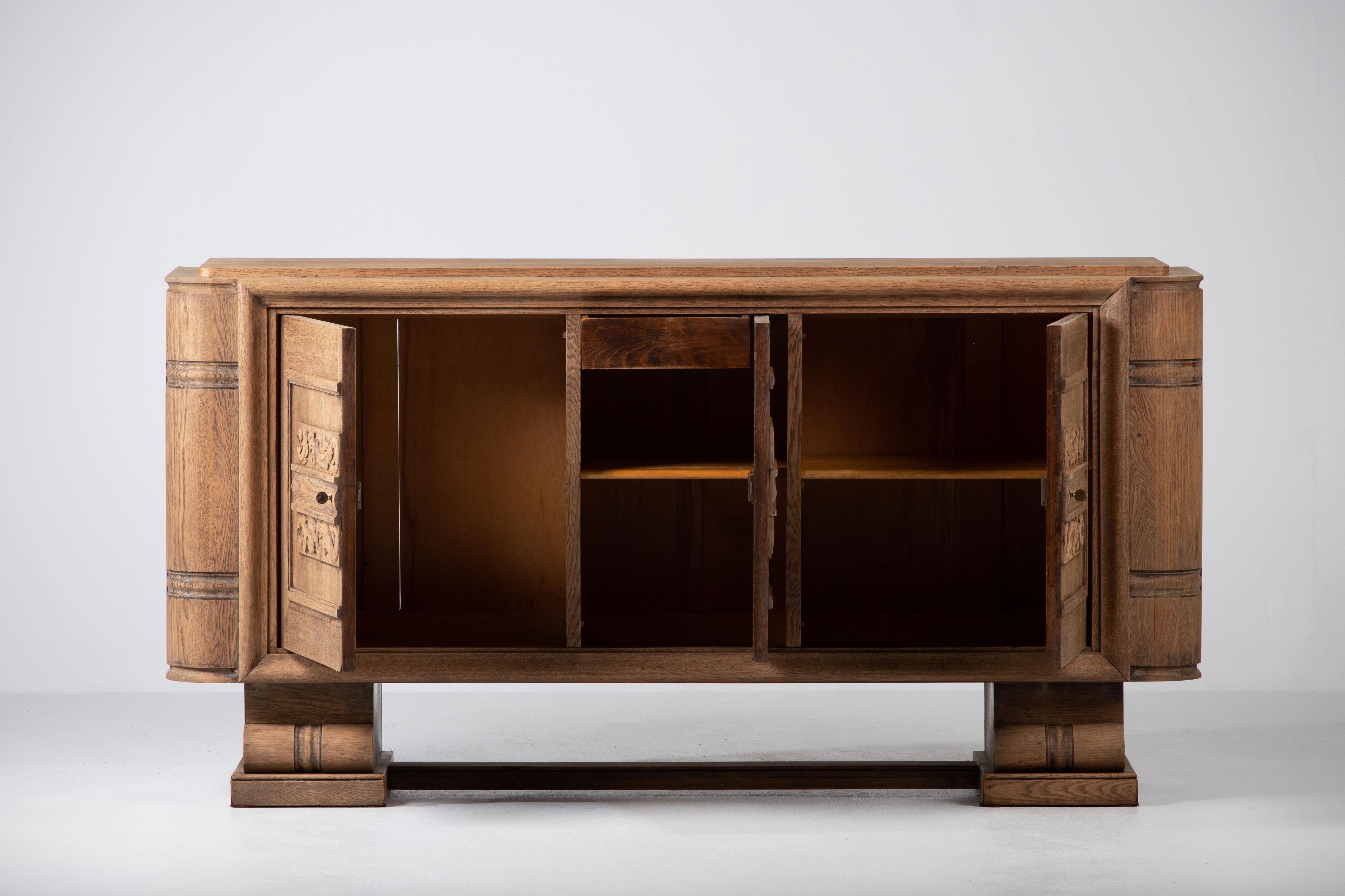 Large Art Deco Brutalist sideboard, France, 1940.
The credenza consists of three storage facilities with a handcarved foliage on the doors.
The refined wooden structures on the doors create a striking combination with the otherwise sturdy and