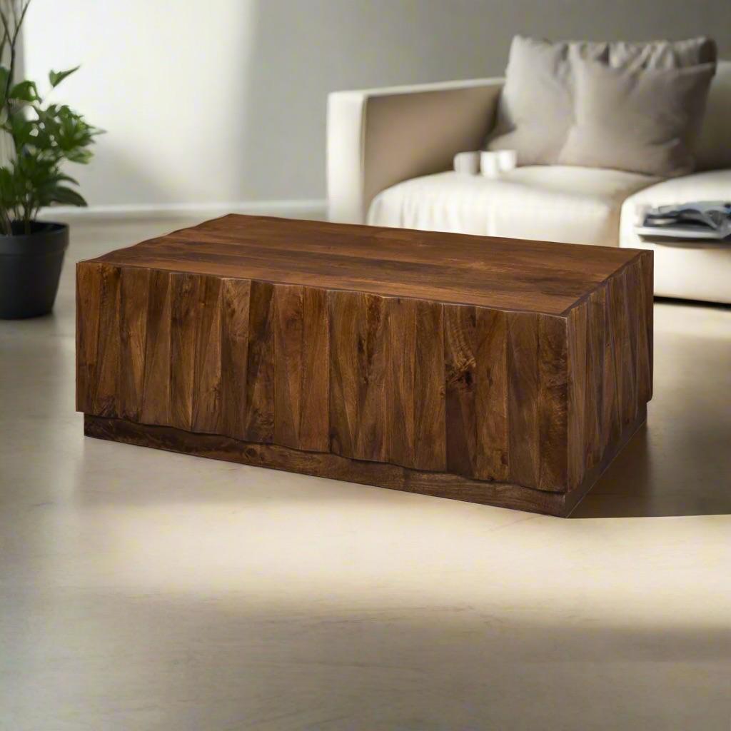 The coffee table makes a commanding statement with its bold sculptural form and faceted surface. Crafted from solid mango wood, the rich brown transitional finish enhances the natural variations of the grain while highlighting the dimensional