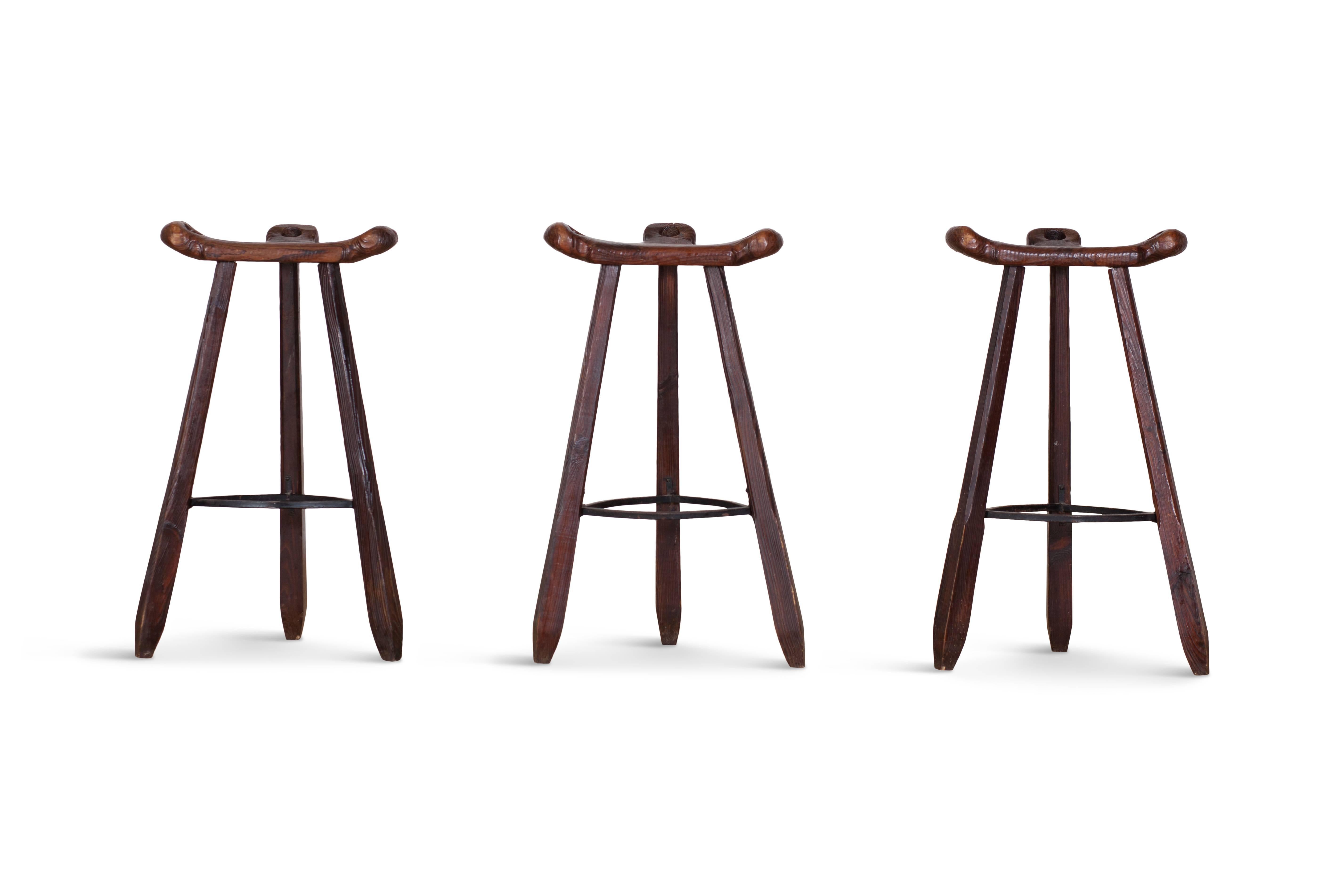 Primitive wabi-sabi set of three ‘Marbella’ bar stools in the style of Sergio Rodrigues, Spain, 1970s.

The curved T-shaped seats have handles on all sides and provided the stools with a stable seat.
The three tapered legs are provided with a
