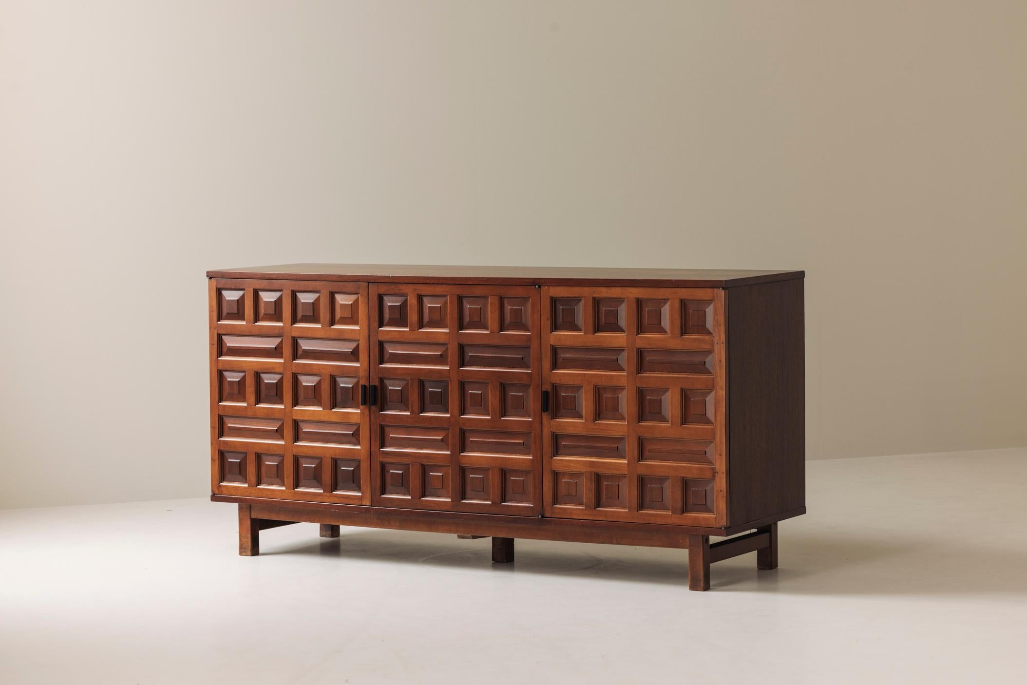 Dieses brutalistische spanische Sideboard aus den 1970er Jahren ist ein wahrer Blickfang und skulptural. Die Fassade aus reichlich gebeiztem Nussbaumholz zeigt eine kühne Abfolge von handgeschnitzten geometrischen Motiven, die dem Stück eine