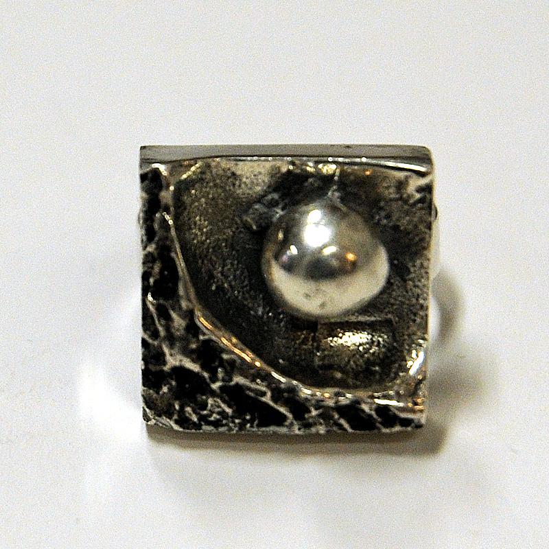 A charming square shaped Finnish silver ring from the 1970s.
This midcentury silverring has a Brutalist design with a crater look and a silver ball in it. Suitable for every occasion. Marked with: 830H NOEB and E.

Measures: Inner diameter 17 mm,