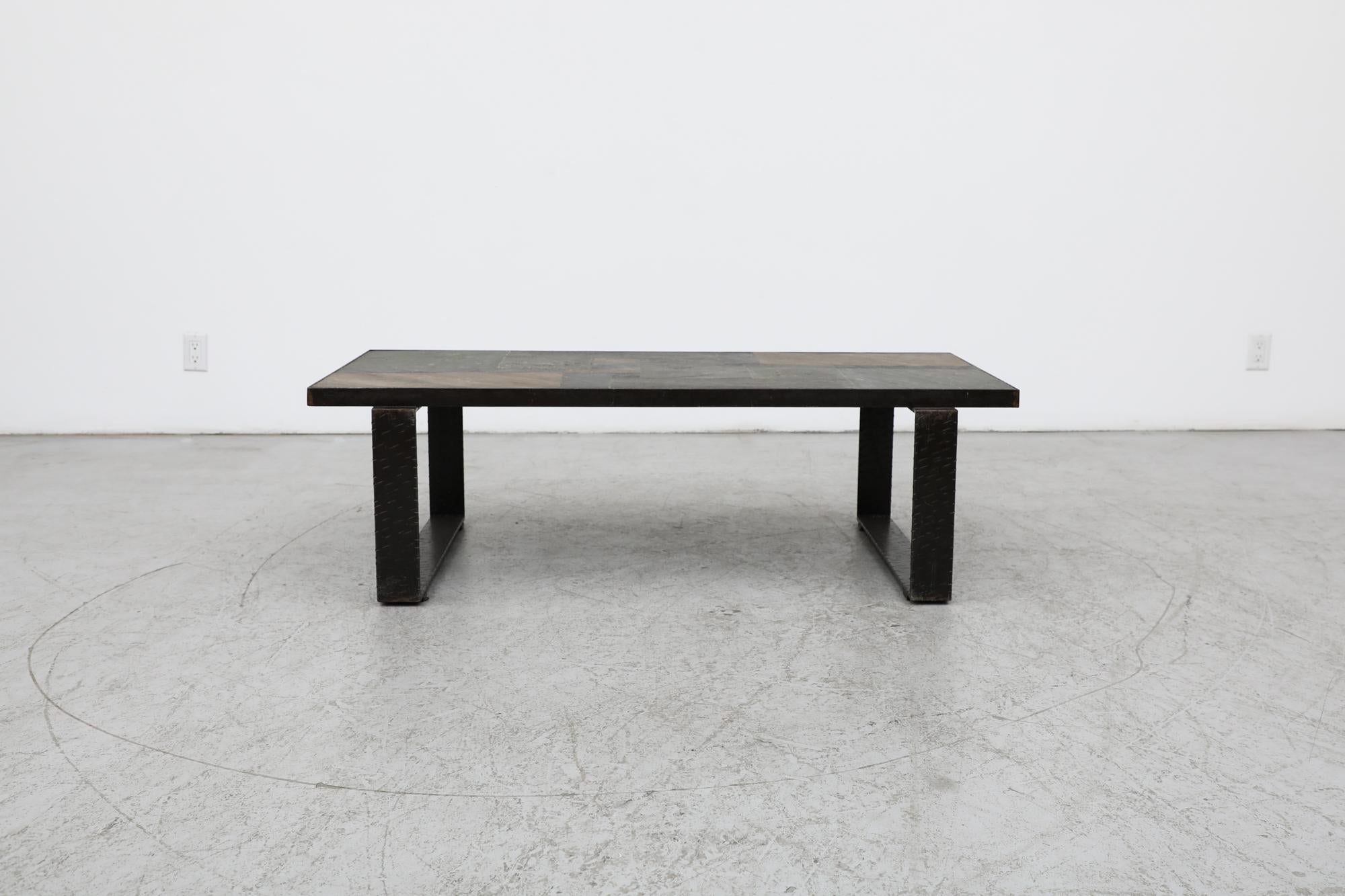Une puissante table basse brutaliste inspirée par le travail de Paul Kingma. Cette pièce présente un captivant plateau en mosaïque de pierre avec une palette de tons bruns, ardoisés et gris, enchâssé dans un lourd cadre en acier. La base