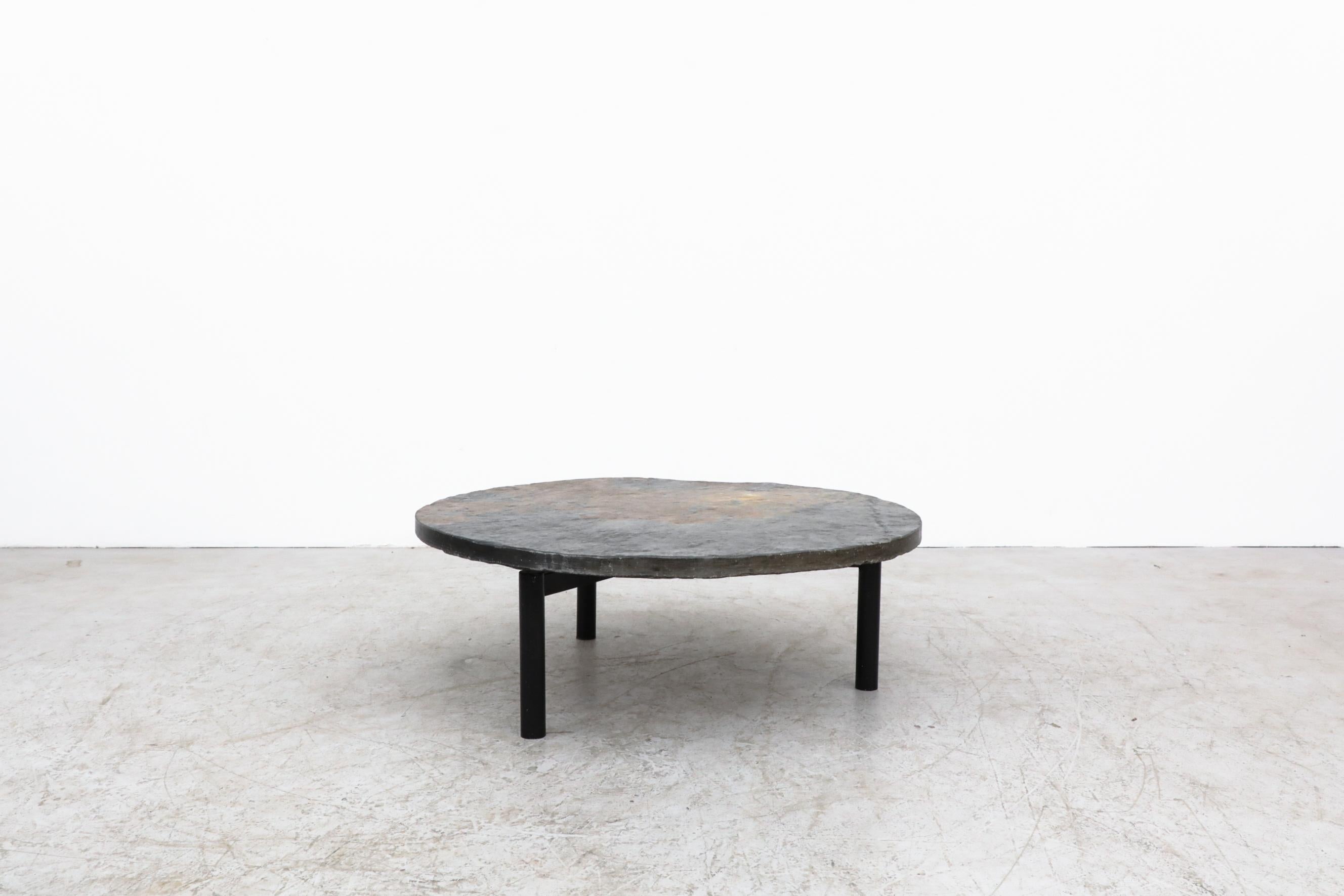'T Spectrum round stone coffee table with black enameled tripod base. Heavy stone slab top with beautiful coloring. Stone has some scratching and chipping. The base has visible scratches as well. Bolts in the frame top act as leveling tools. In