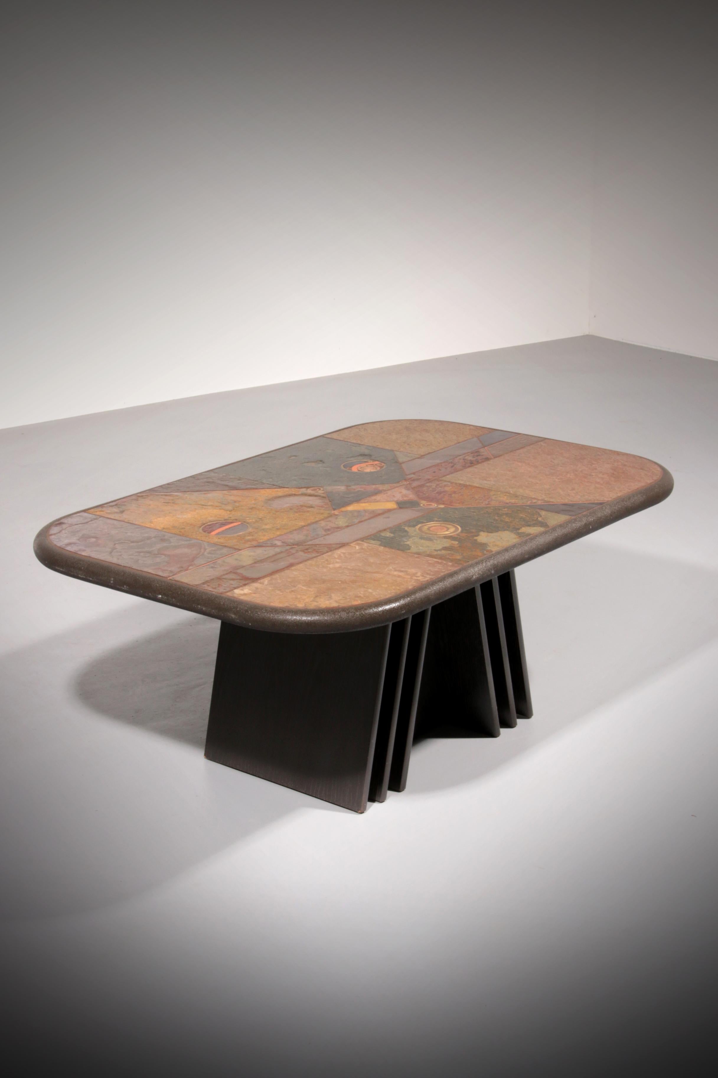 A beautifully crafted stone coffee table inspired by the style of Paul Kingma. The tabletop showcases a striking mosaic of natural stone, accented with brass and embedded coins that add character and uniqueness. The piece rests on a solid hexagonal