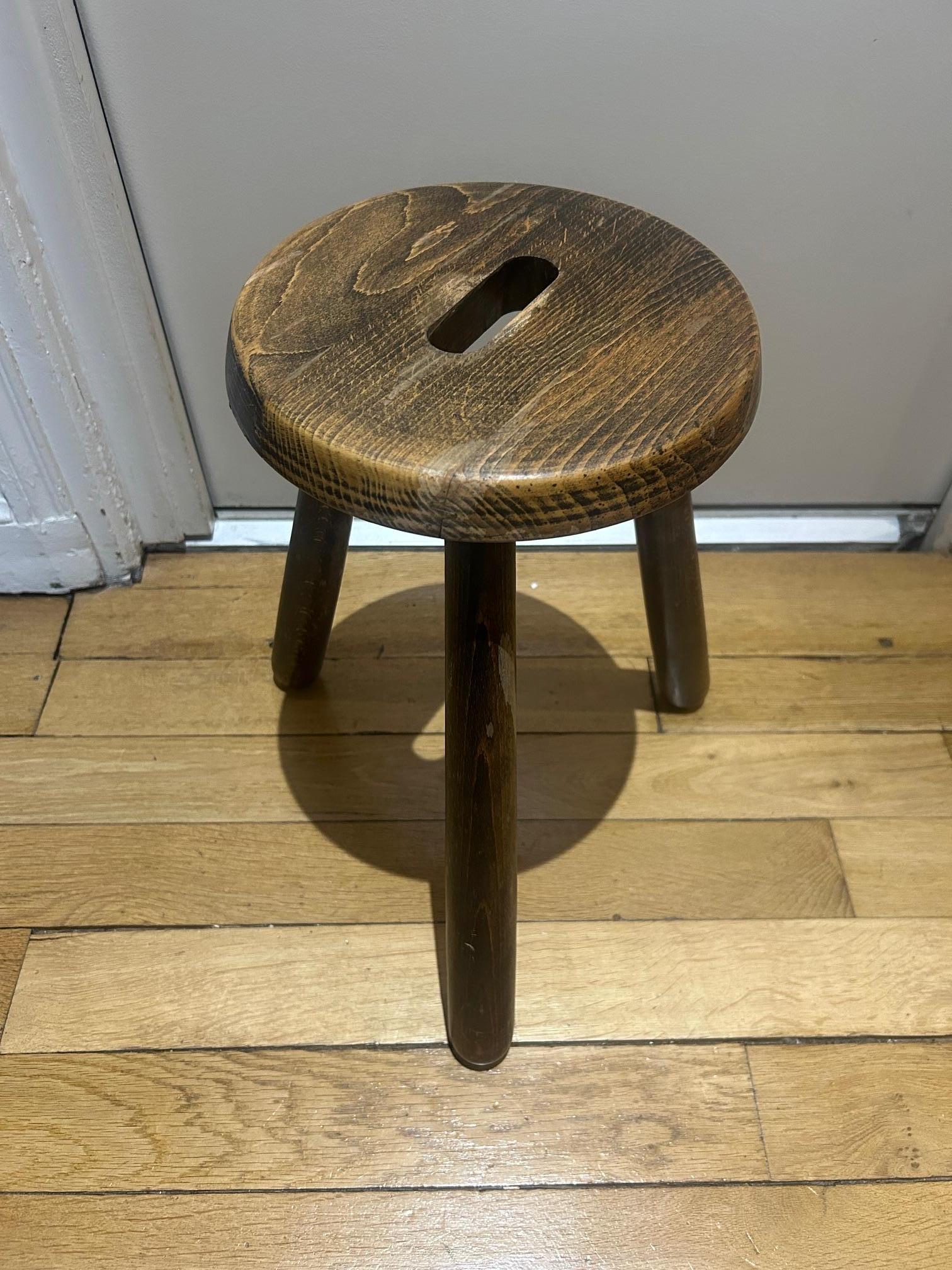 A wooden three-legged stool with a strong brutalist vibe.
It has a chunky, sculptural look, letting the natural grain and imperfections of the wood stand out. 
The legs are simple and sturdy, giving it a slightly raw, handmade feel.
 It’s a