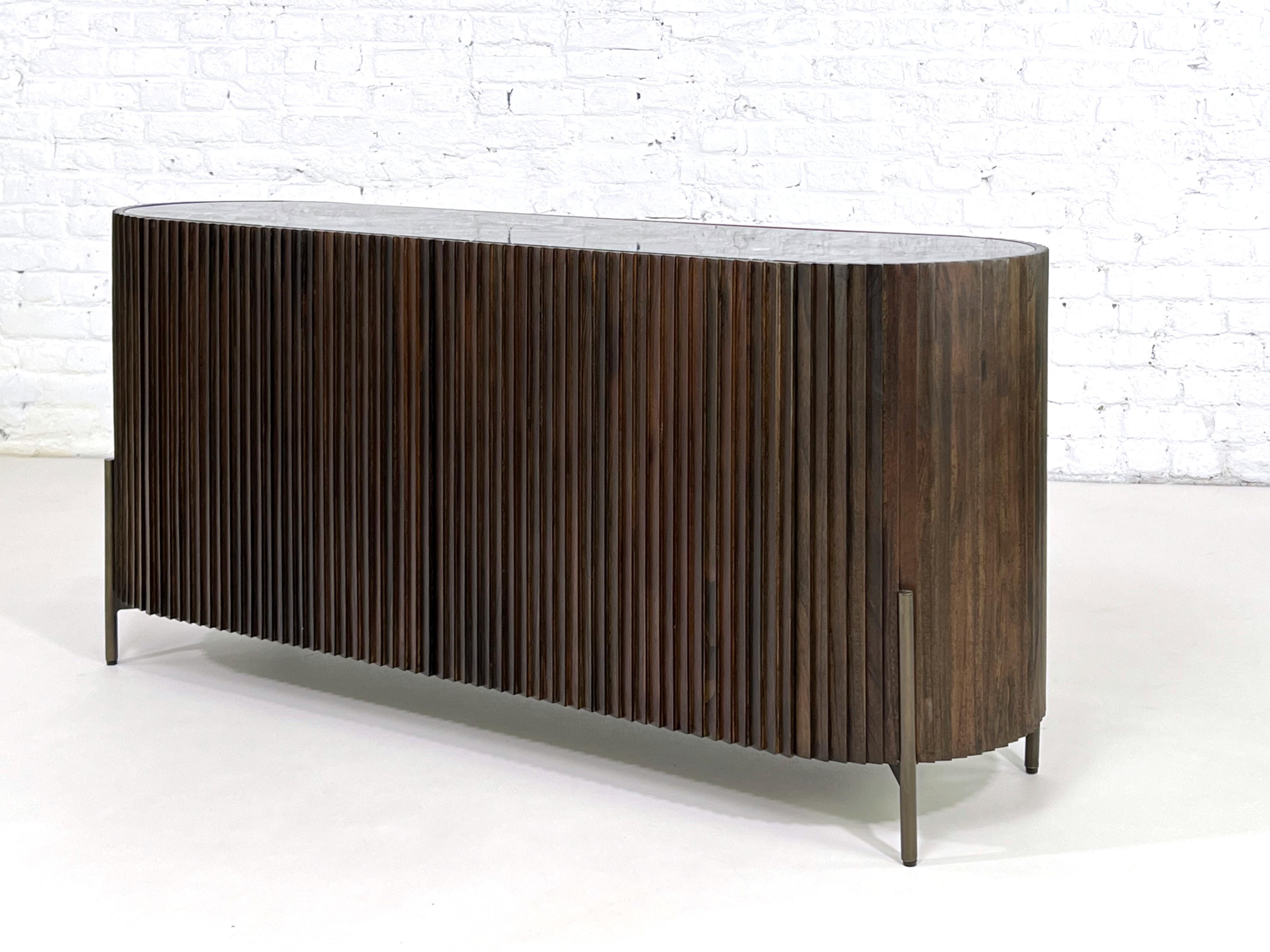 Graphic and Brutalist style Mid-Century Modern design oval shaped sideboard in wooden structure with a bevelled nero marquina marble stone top and brush brass legs finishes.