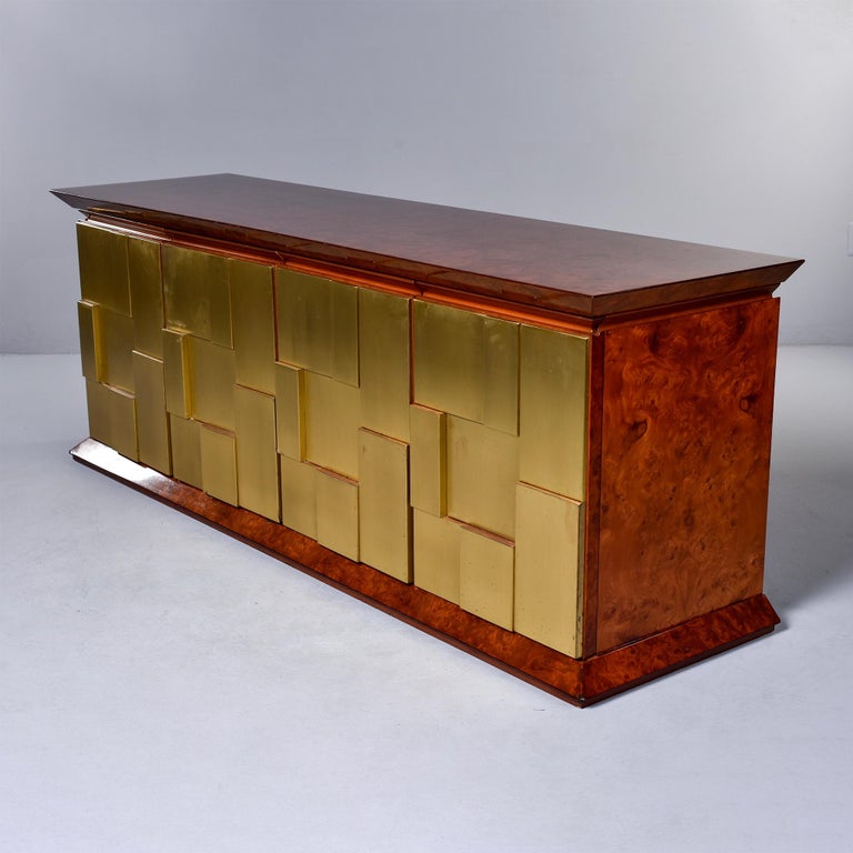 Found in England, this circa late 1960s buffet cabinet has burl wood top, sides and base with a striking Paul Evans style brutalist paneled brass face. Interior is finished in rosewood veneer with open storage and a single internal shelf on one side