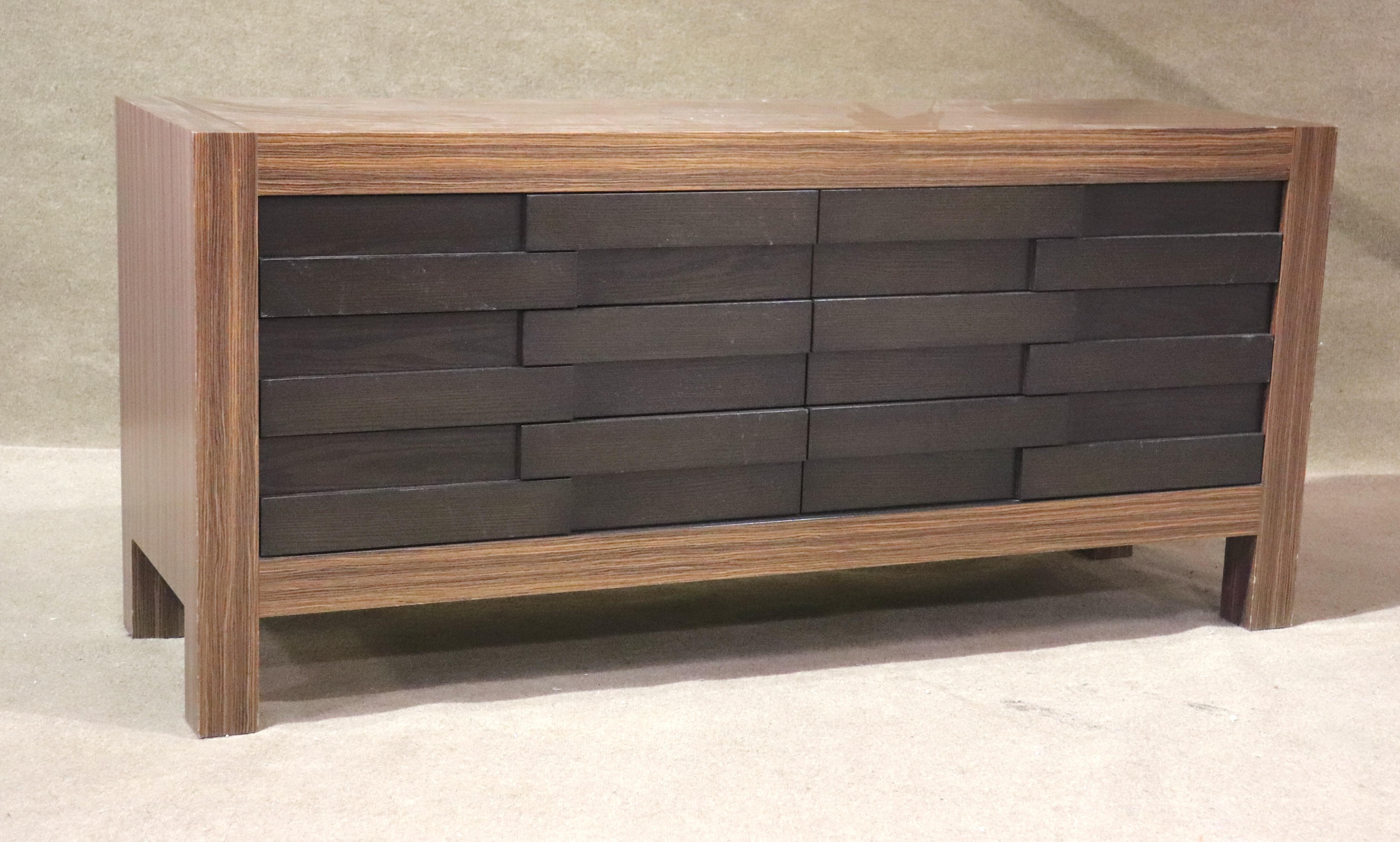 Comò lungo con frontale in stile brutalista o intrecciato. Sei ampi cassetti in legno scuro, circondati da una cornice in ebano macassar.
Si prega di confermare la posizione NY o NJ