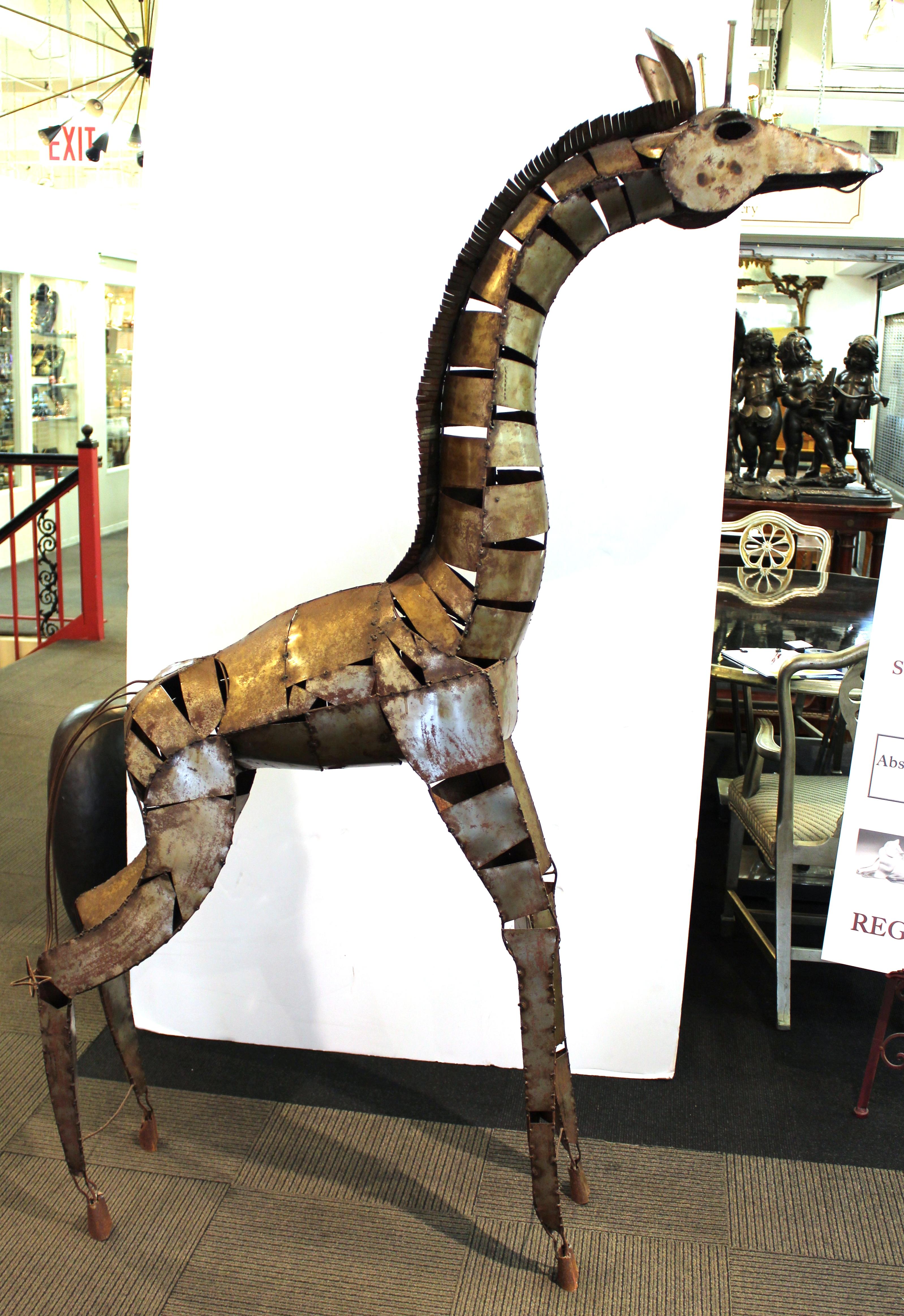 Brutalist style sculpture of a standing giraffe, made of welded metal pieces. With its height of almost 80 inches, the sculpture has a towering presence and is suited both for indoors and outdoors. Some wear and patina to the metal surface.