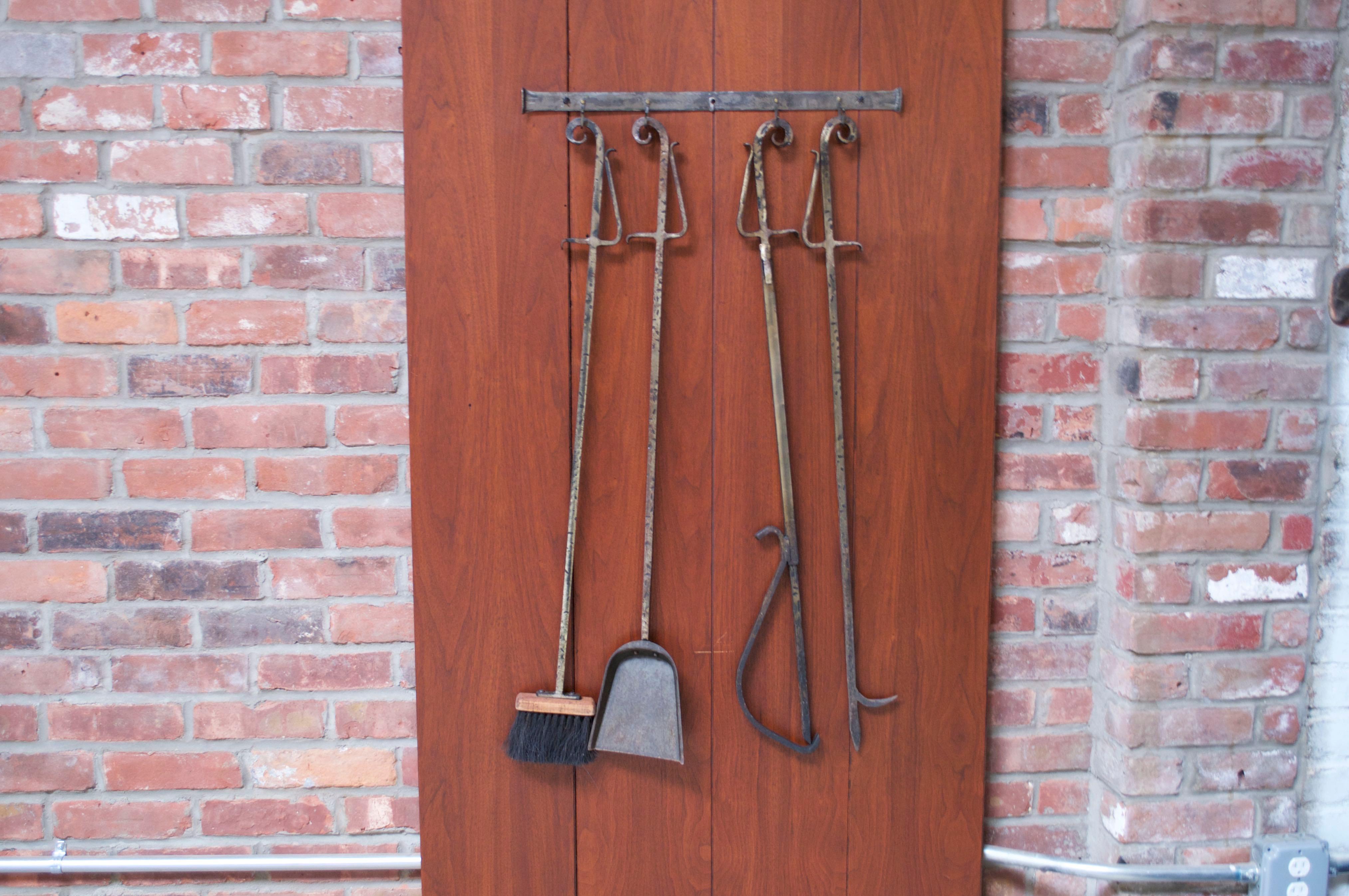 Circa 1970s / 1980s fire tool set including poker, log holder, brush, and shovel with wall-mounted holder. Nice texture with hammered detail to the forged iron with gilt finish. Paint loss in places / patina from age use. Remains in good, vintage