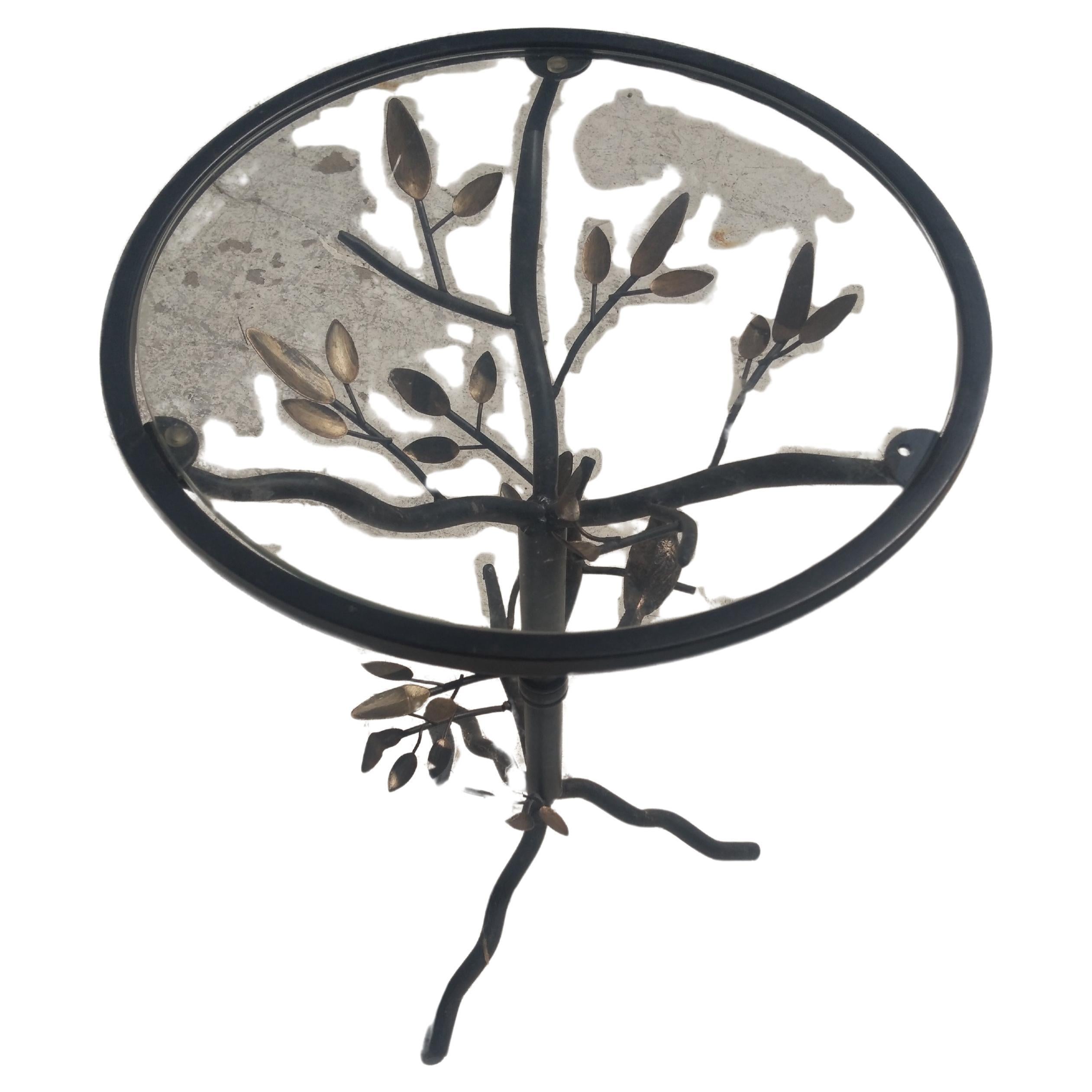 Cette table est fabriquée dans le style brutaliste. Il est en métal patiné. La base est un arbre avec des branches et des oiseaux. La partie supérieure est en verre ajusté.