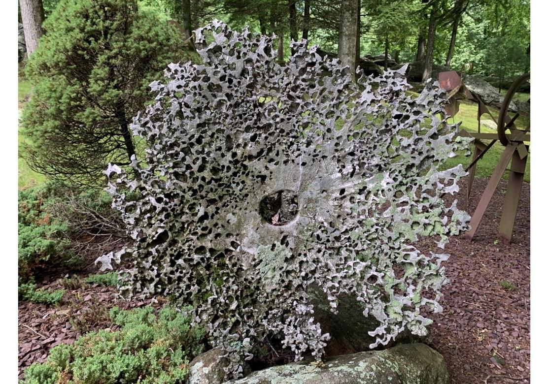 Striking Brutalist sculpture suitable for the Garden by multidisciplinary artist Norma B. Flanagan. A large scale abstract flower like piece made of slag metal set at an angle. It is pierced overall with irregular edges and a hole in the center. The