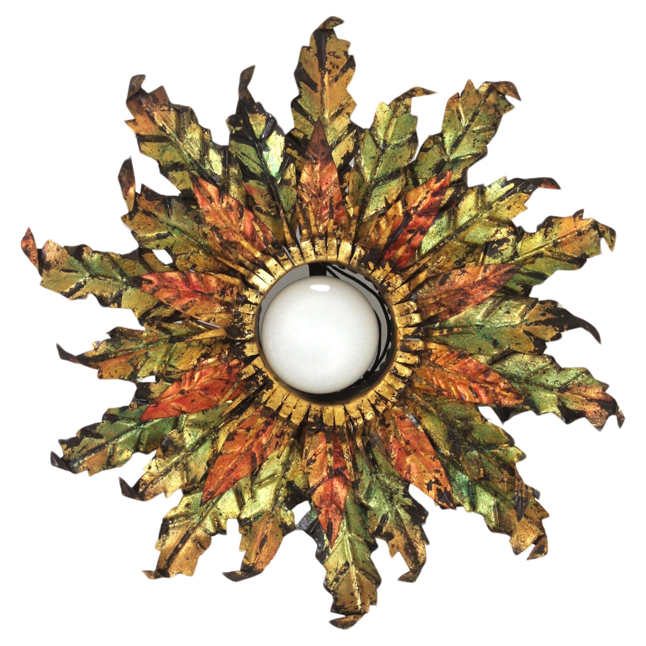 Flower shaped sunburst flush mount, gilt iron, gold leaf, Spain, 1950s.
Eye-catching triple layered foliage light fixture made of hand-cut iron leaves surrounding a central exposed bulb. Finished in gold leaf gilding in three tones, golden, red and