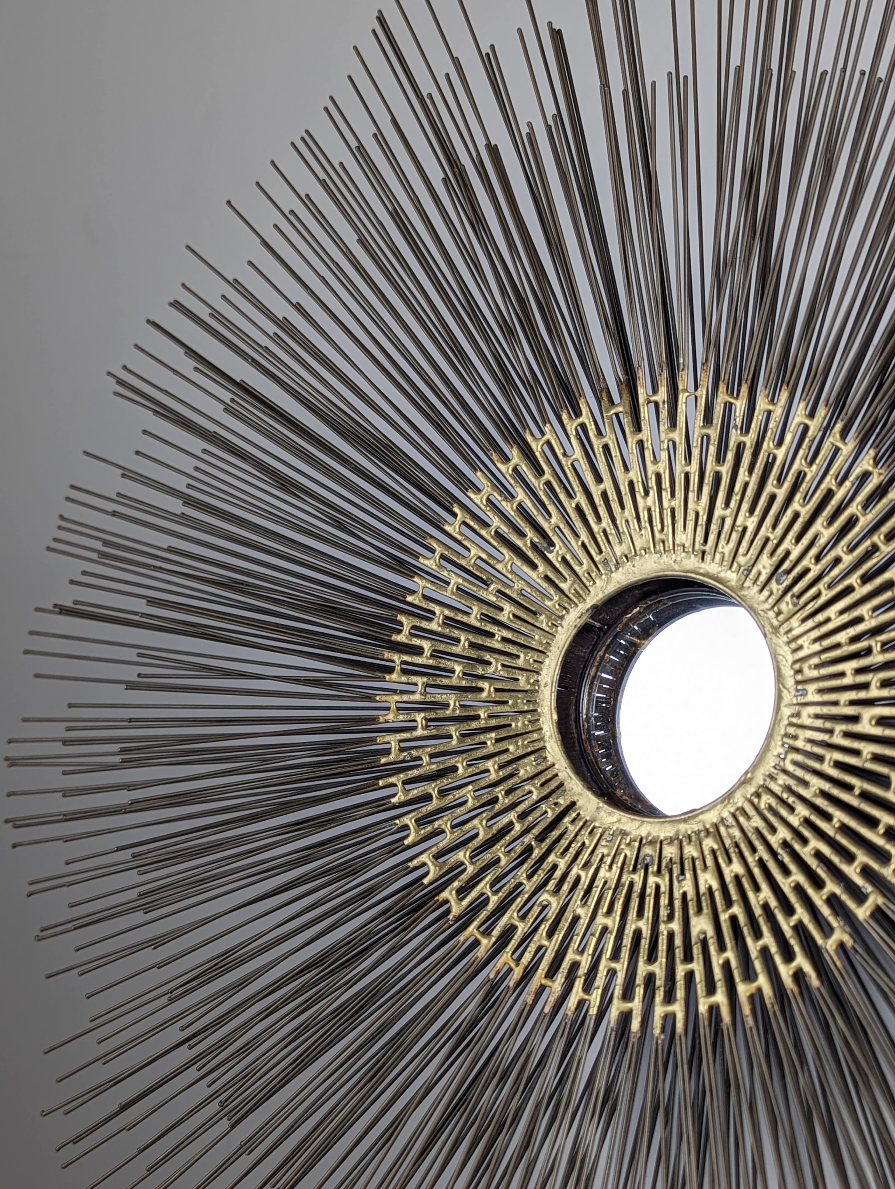 Exciting Brutalist wall sculpture from the 1970s featuring the unmistakable sunburst design by the acclaimed artist William Friedle. This captivating piece showcases a central mirror surrounded by three layers of rays, with the rod design imparting