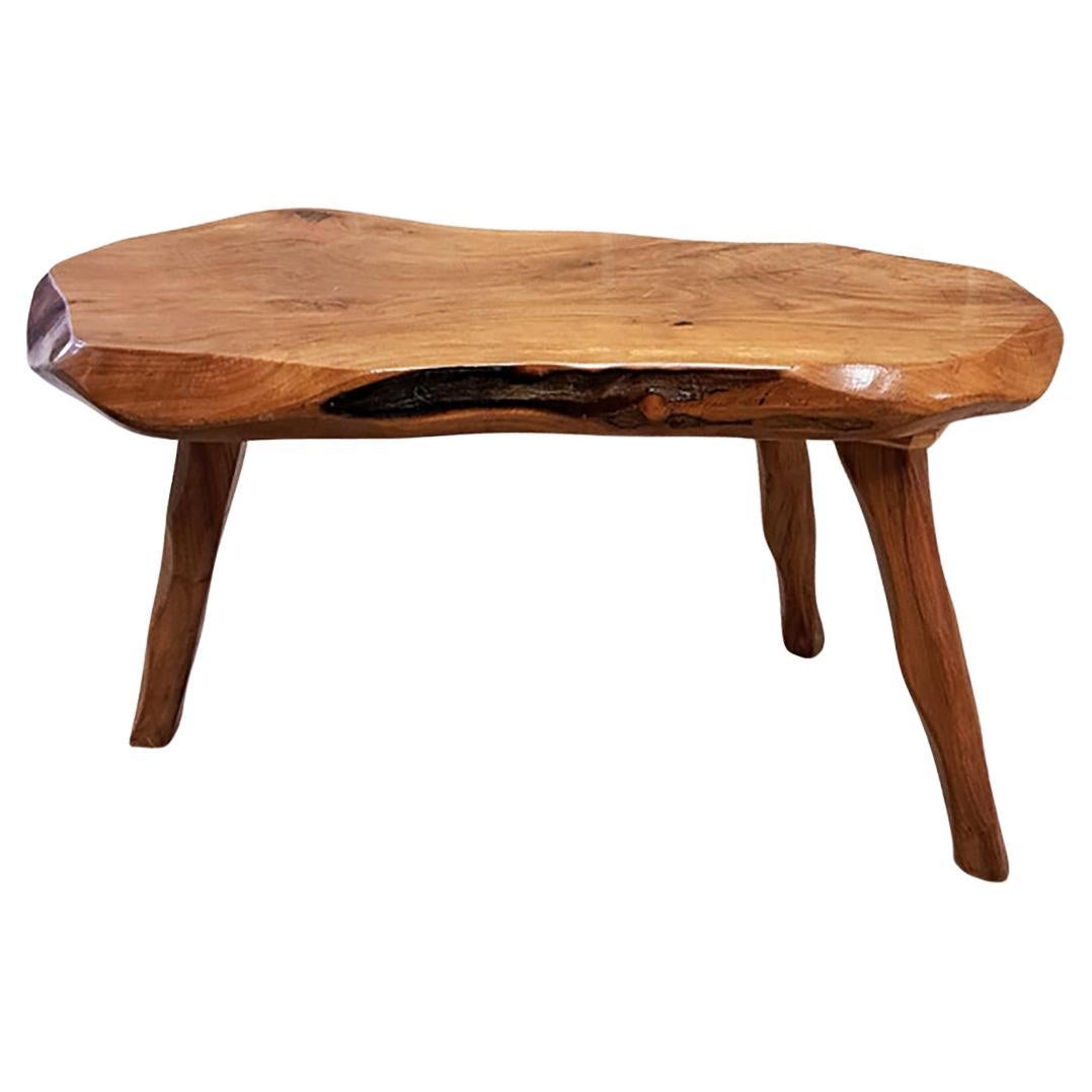 Table basse ou d'appoint en bois brutaliste fabriquée en France dans les années 1950. Fabriquée à partir d'une plaque massive d'orme verni, cette pièce sculpturale repose sur trois pieds tripodes de forme organique, mettant en valeur le grain