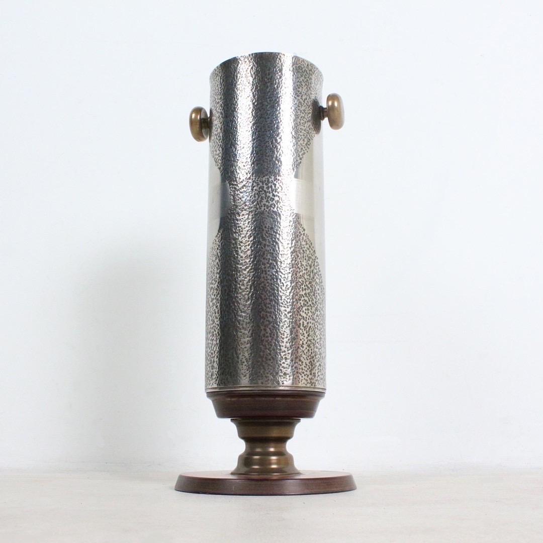 Introducing a Striking Brutalist Vase with Industrial Charm

Presenting a unique piece of art, this Brutalist vase is sure to captivate with its rugged and industrial aesthetic. Crafted from stainless steel with brass fittings and a teak wood base,