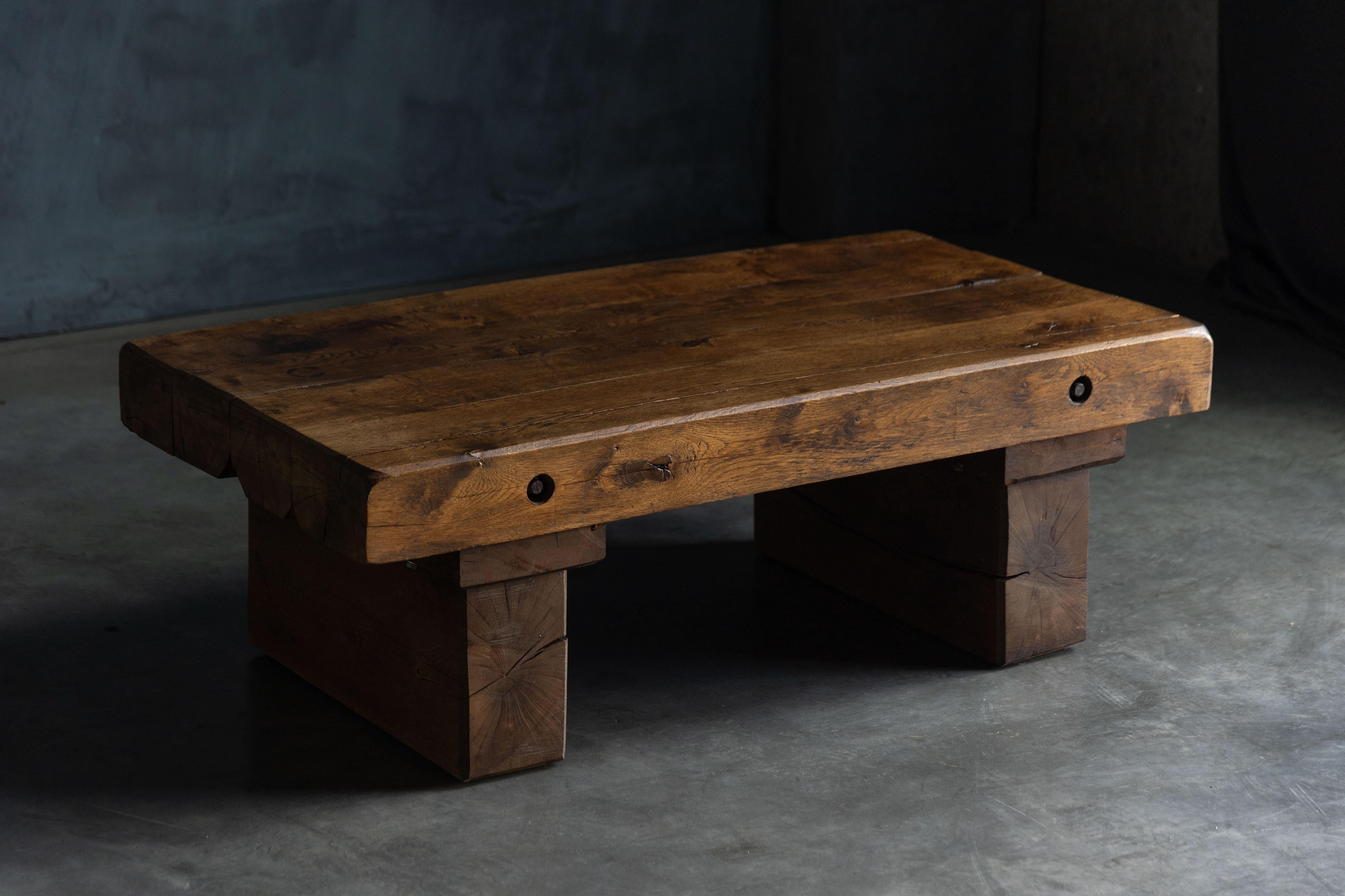This rustic brutalist coffee table captures the raw beauty of minimalist design with its bold, two-legged base and solid wood construction. The rectangular surface offers generous space, perfect for showcasing books, artful curiosities, or simply