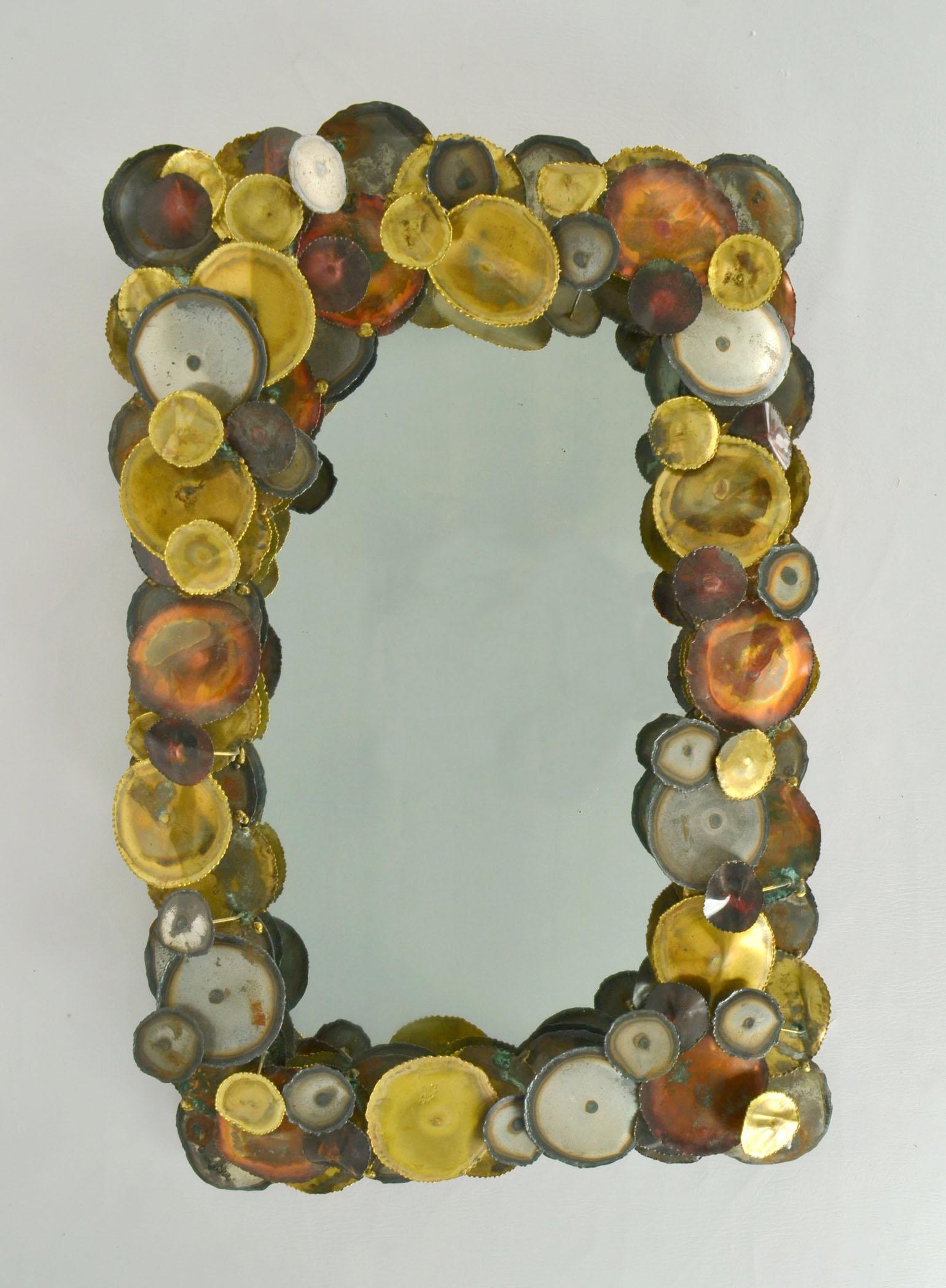 Brutalist rectangular wall mirror in the style of Curtis Jere with relief border in hand torched circles of brass and mild steel suspended randomly around the mirror. The mirror is made in the 1970's and is signed FG.
