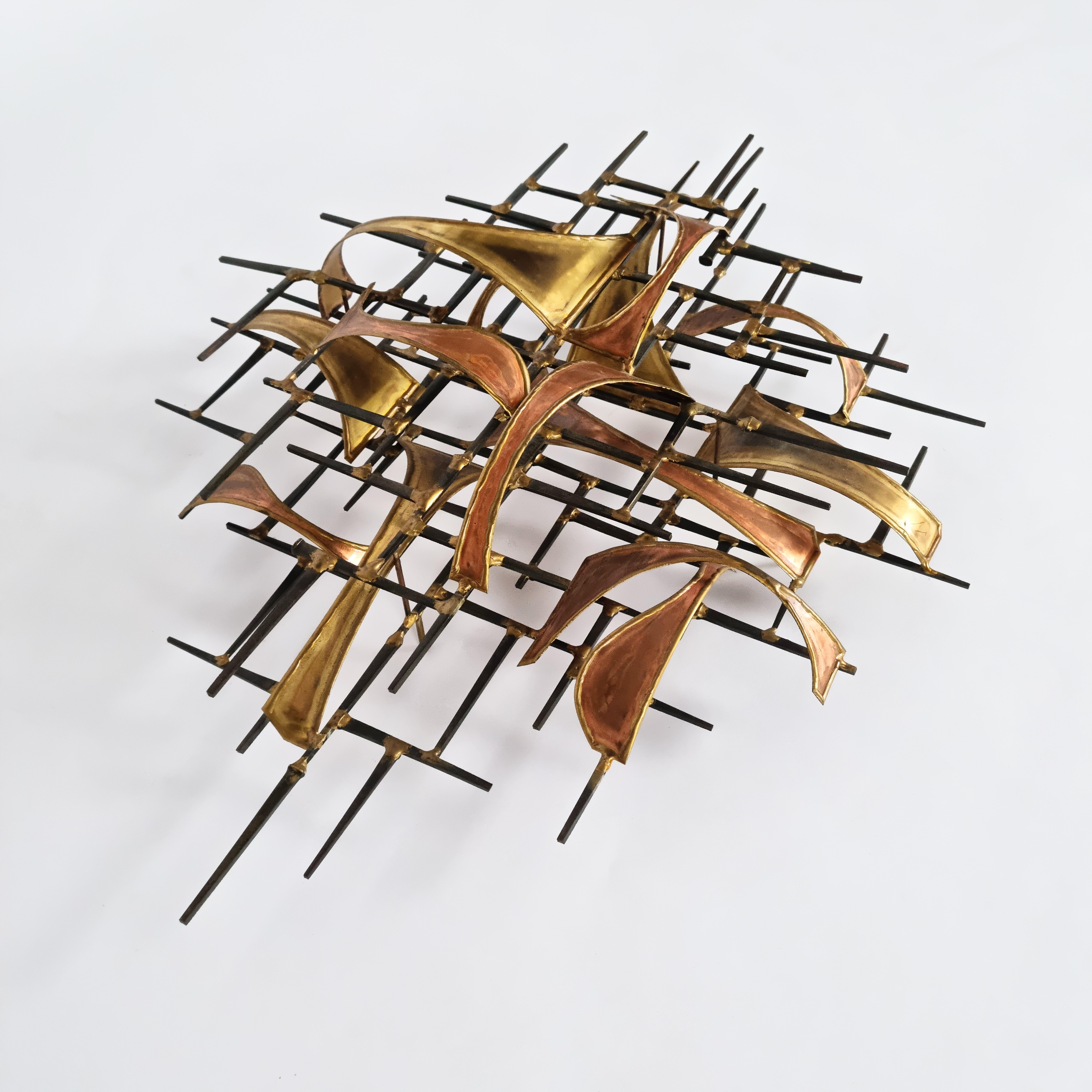 This striking Brutalist wall sculpture by Higgins is a masterful composition of brass and copper. The structure is crafted from thin metal rods, creating an intricate framework, while the facade features delicate, ribbon-like, two-tone bent metal