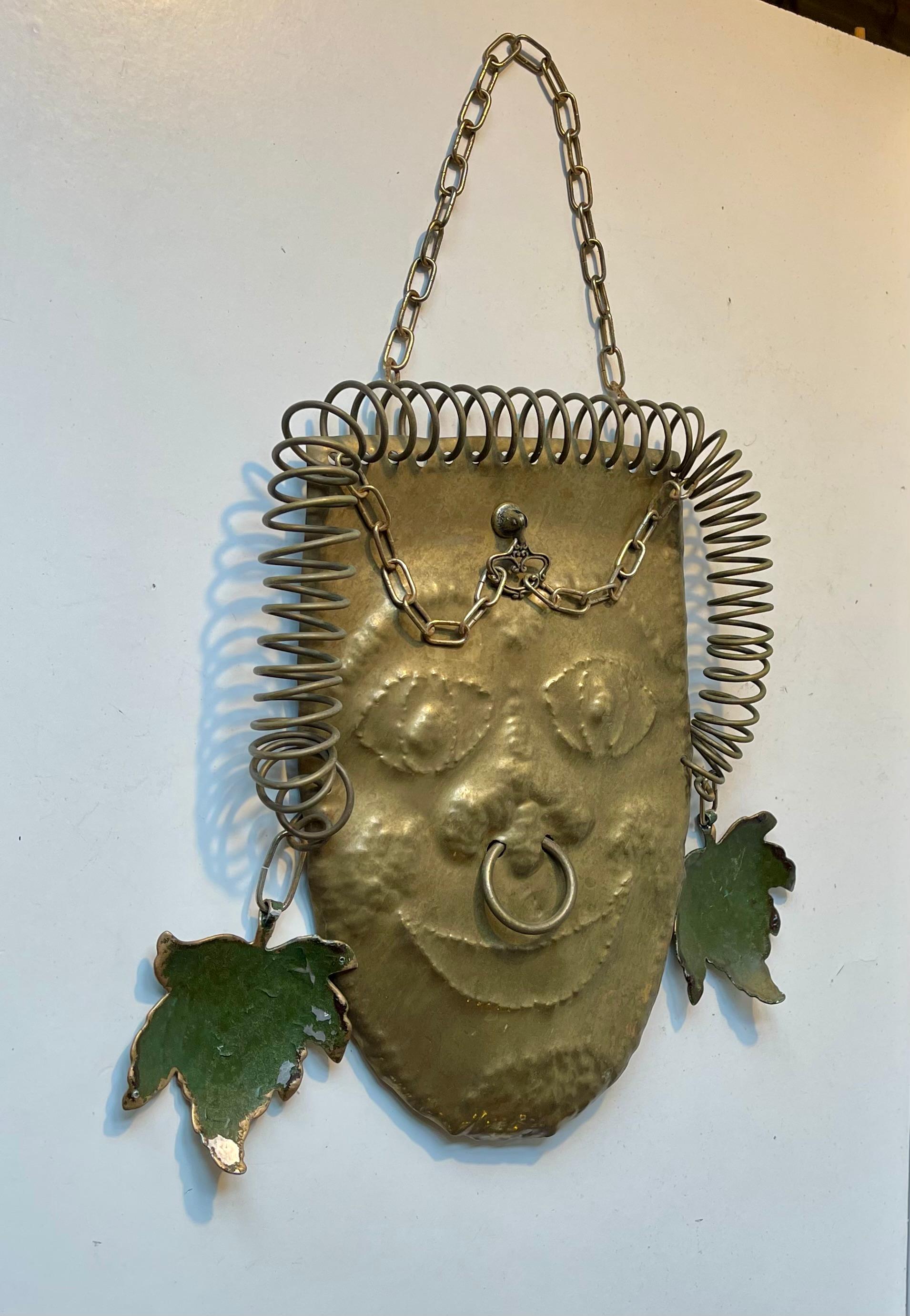 A one of a kind chain-suspended warrior wall head in brass. It made entirely from re-purposed/recycled parts. It features spiraling 'spring-hair', acid-cut earrings, forehead-jewelry and nose-ring. It's signed by an unidentified Danish Sculptor -