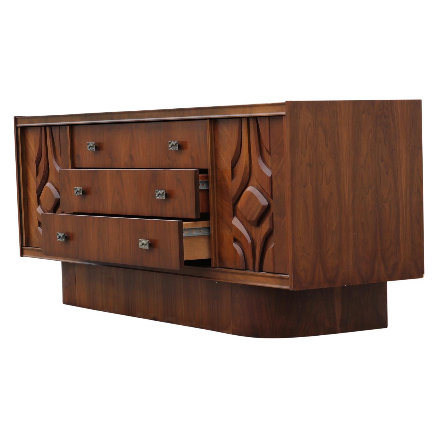 Carved walnut sideboard or credenza in the style of John Widdicomb. The sideboard has three large pull out drawers and two swing out cabinets on each side of the drawers. The knobs on the drawers are beautifully beveled.