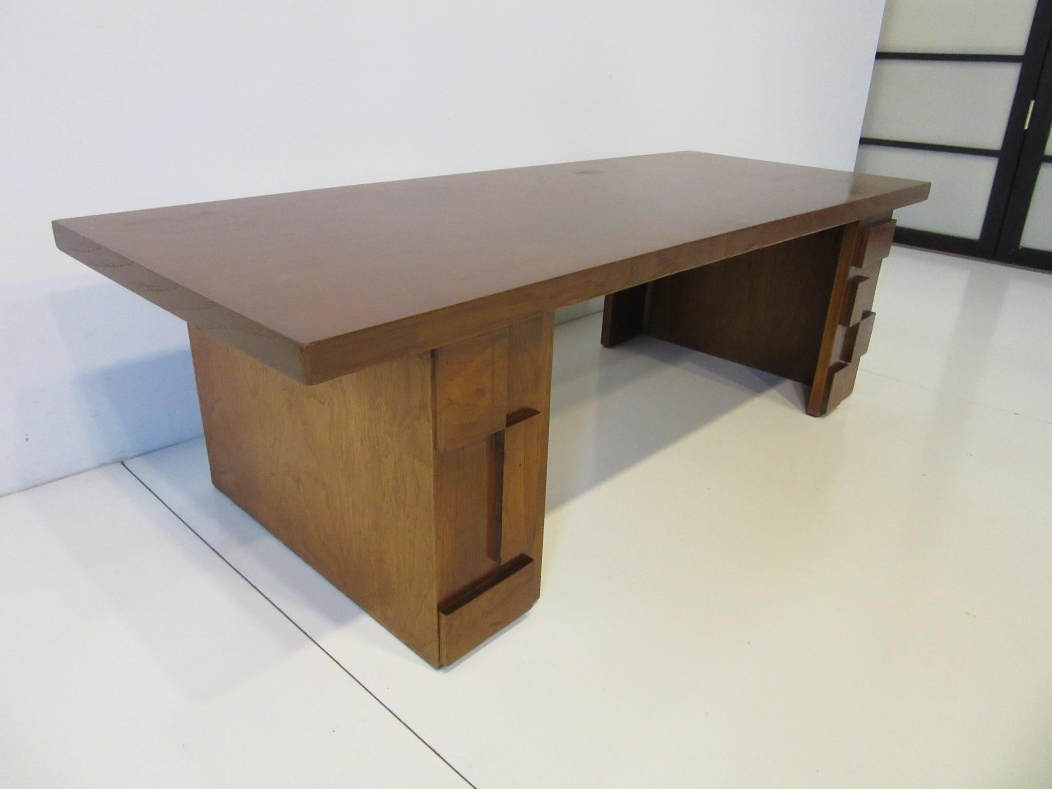 A dark walnut toned coffee table in the Brutalist style with applied blocky forms to the legs heavy graining to the top and a contrasting wood grain boarder trim. Manufactured by the Lane Furniture Company Lane Altavista.