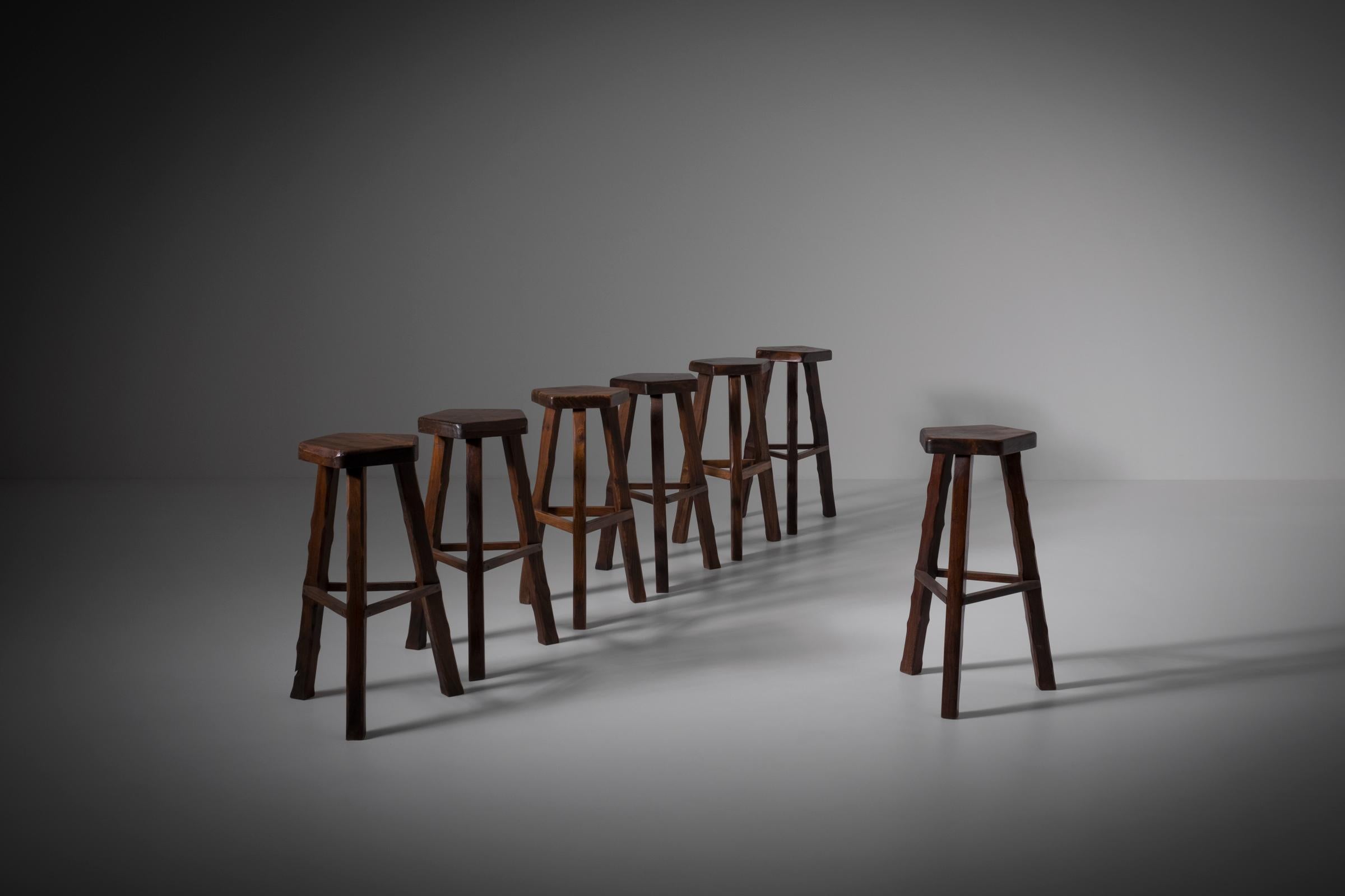 Set of seven sculptural bar stools, France 1960s. These bar stools are often attributed to Olavi Hänninen but are actually a French production of the 60s. The stools are constructed out of dark stained Elm wood with nice warm tones. Every single