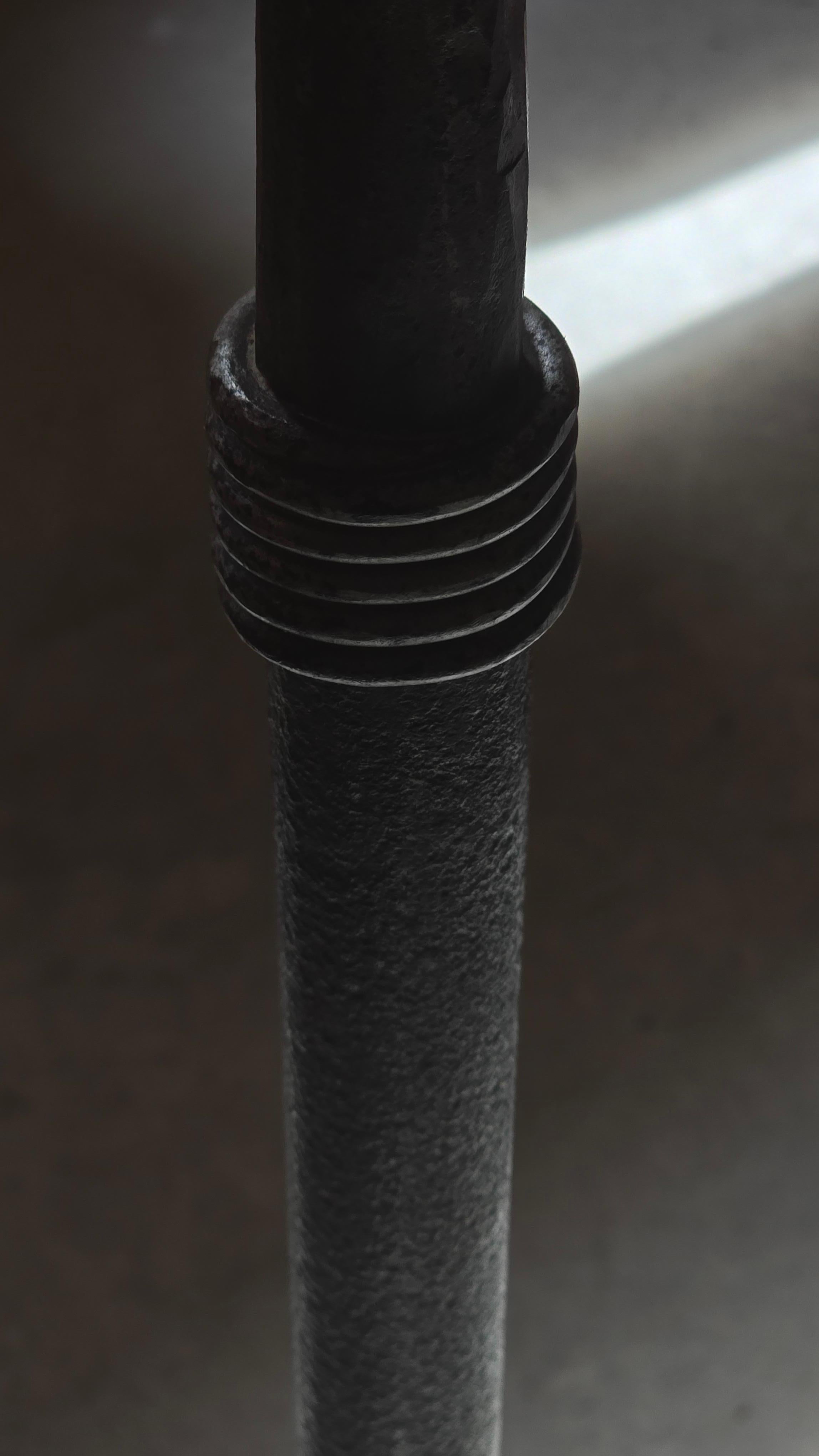 A tall and sculptural floor candleholder in hand-forged iron, France, circa 1960. Characteristic of the Brutalist aesthetic, this piece features a slender, tapered central shaft adorned with a bold annular ornament at mid-height. The base rests on