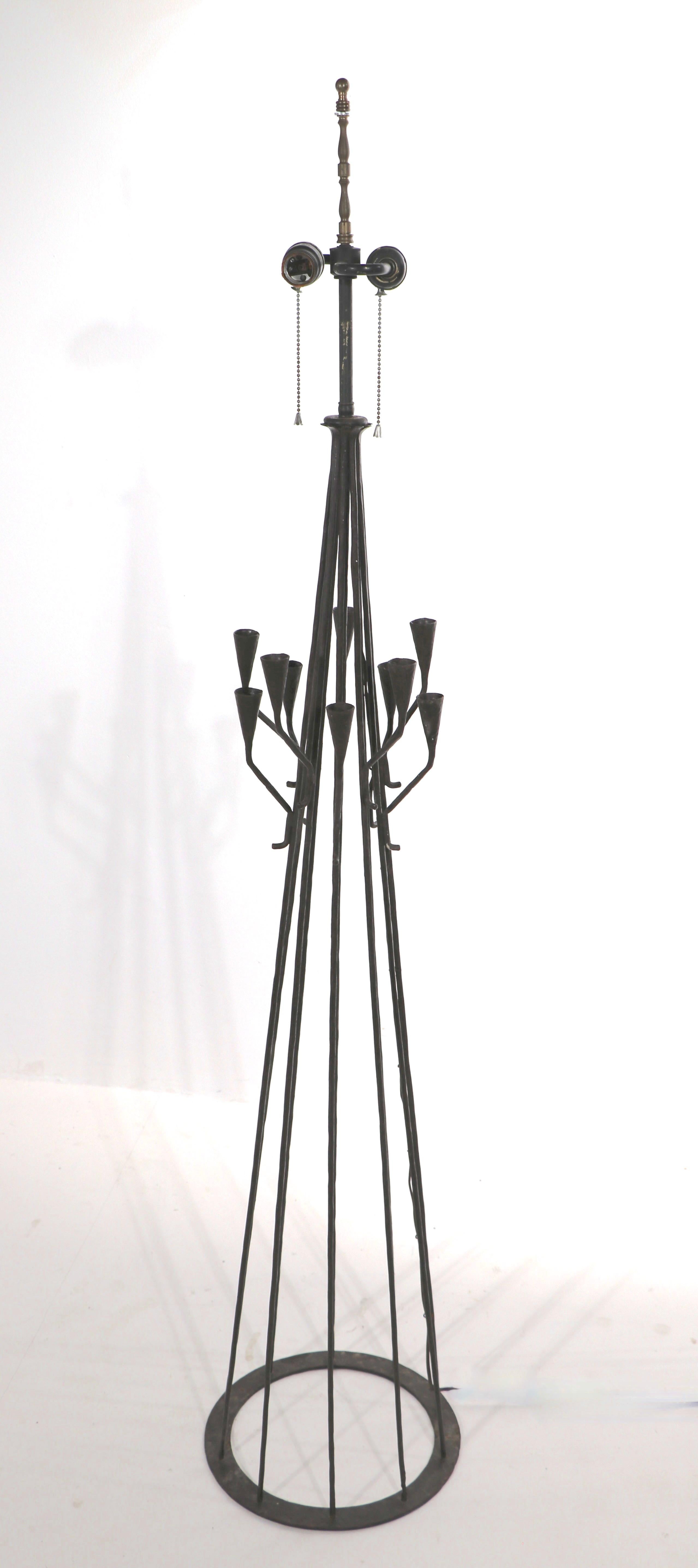 Interessante lampada da terra in ferro battuto, con bracci a candela che si estendono dal pezzo centrale principale. La lampada ha due prese di dimensioni standard (funzionanti). Marchio Made in Portugal, impresso sulla base circolare in metallo. Il