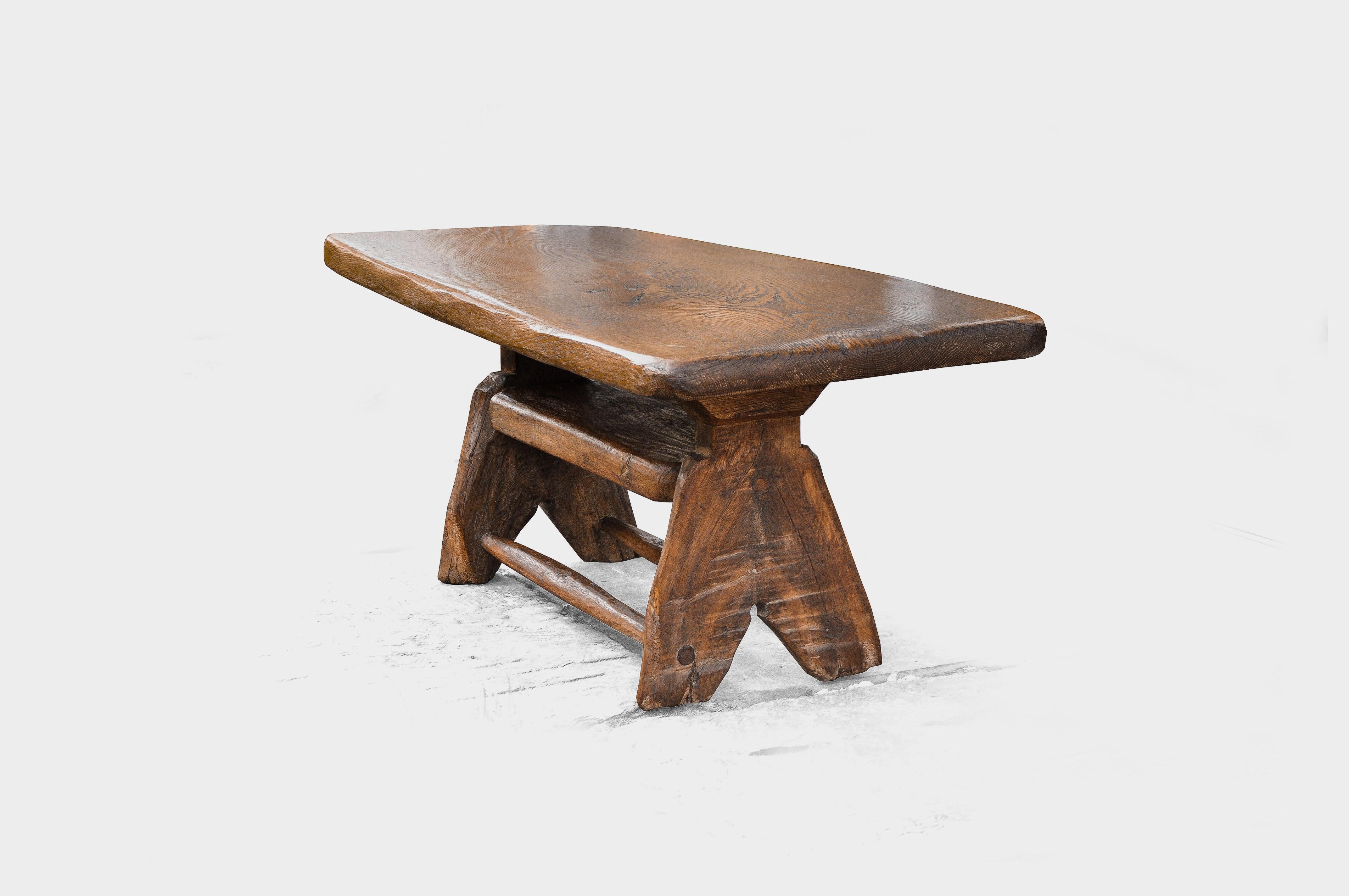 Brutalistic, handmade table made of stained oak, with a 5 cm thick solid oak leaf made of a single piece of unglued wood. On the underside there is a shelf and two carved cross struts, which give the table the necessary stability to also be used as