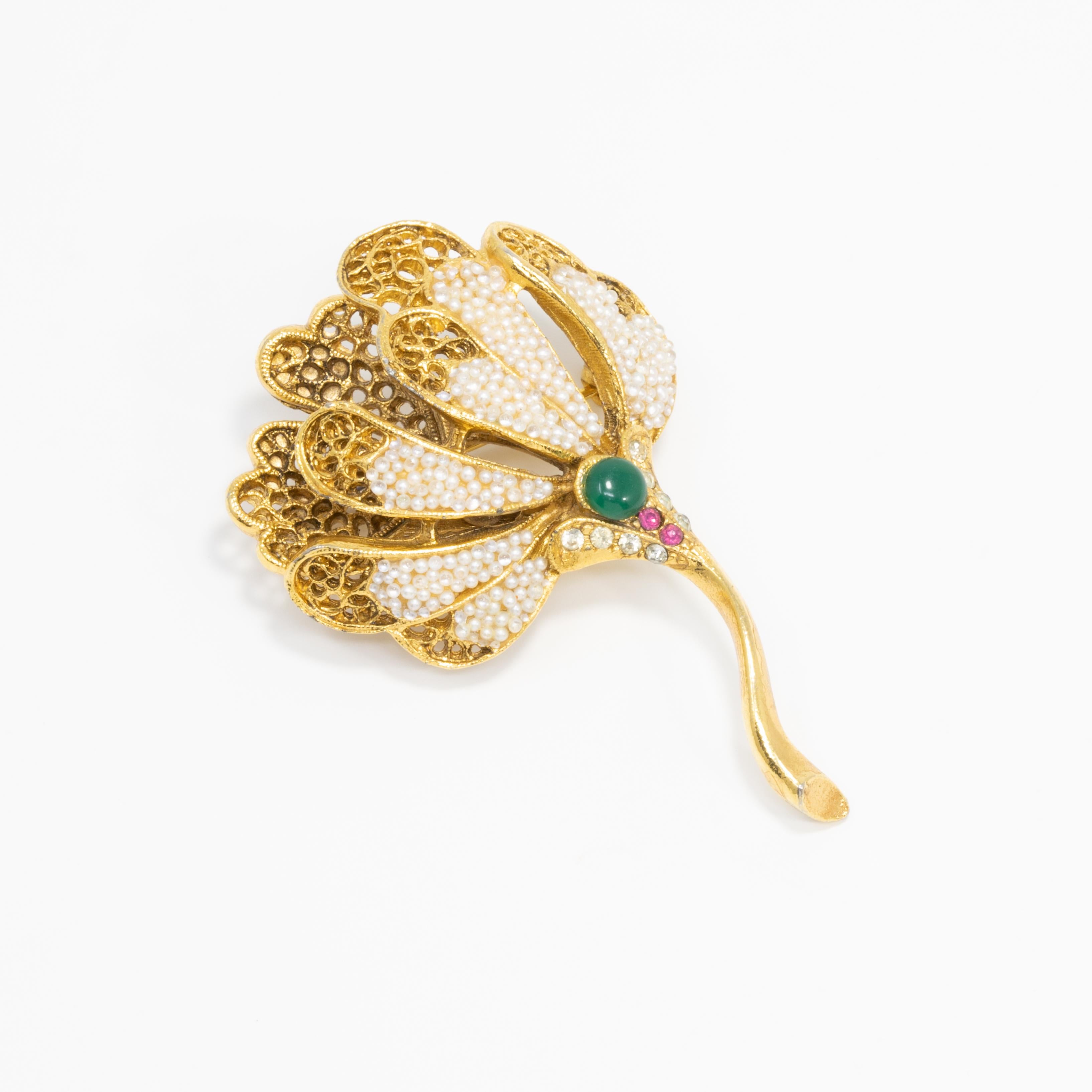 A regal-looking pin brooch by BSK. This gold-tone filigree flower is decorated with white beads, a single emerald-colored cabochon, and rose crystals.

Mid 1900s.

Hallmarks: BSK (Benny Steinberg, Slovitt and Kaslo)