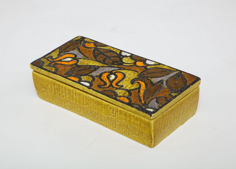 Mustard yellow ceramic box with a contrasting stylized floral pattern lid in umber, orange, yellow, and white. Signed.