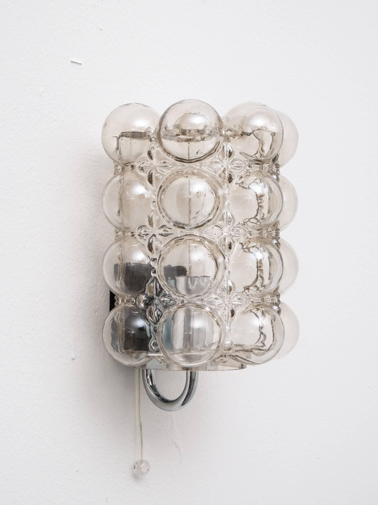 This bubble glass and chrome wall sconce was designed in the 1960s by Helena Tynell for Glashütte Limburg, Germany. The lampshade is made of clear glass and a bubble pattern.

NOS! This light has never been used and is new old stock from a closed