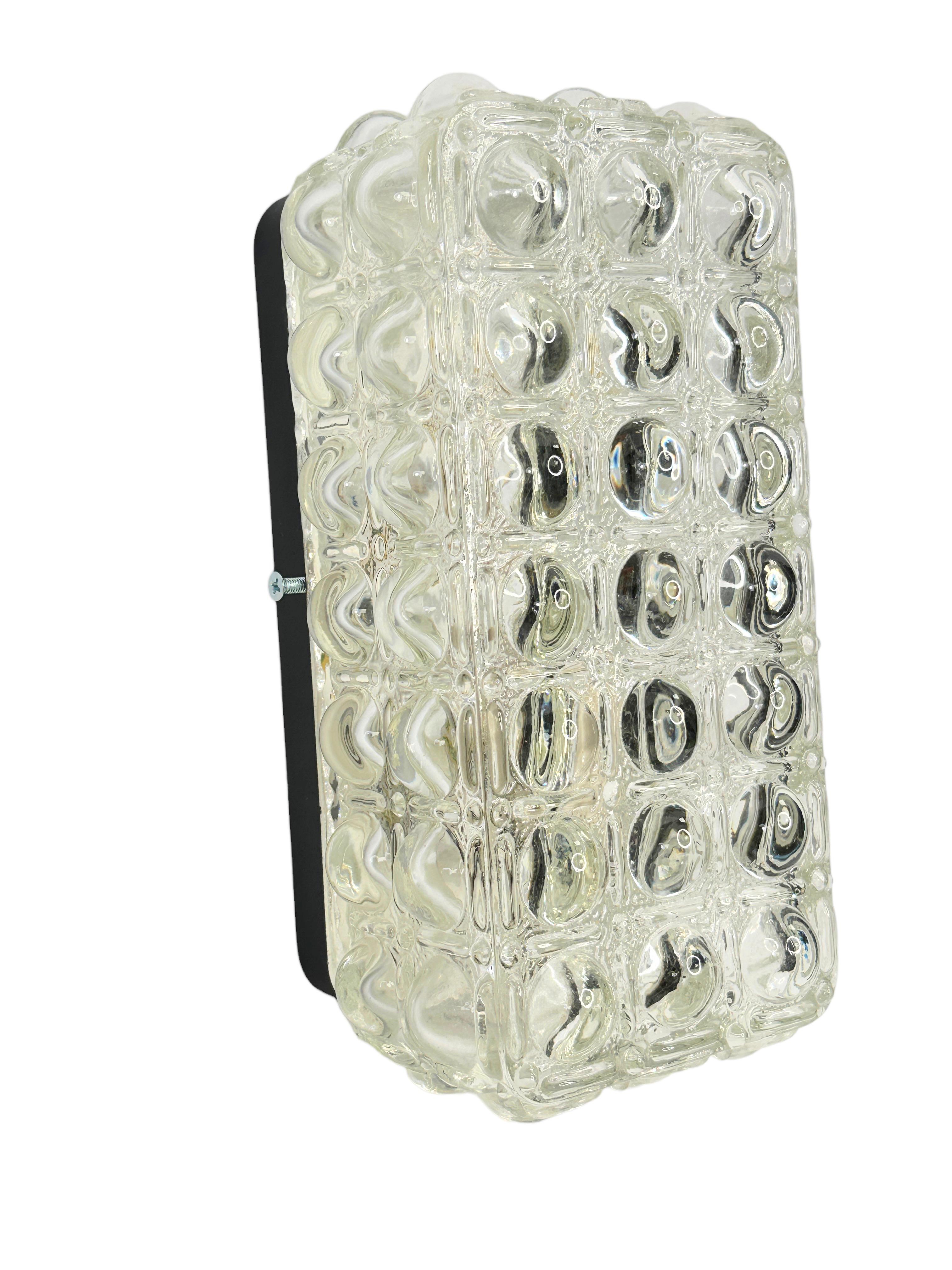 Petite sconce manufactured probably by Glashütte Limburg. It is an clear glass on a black lacquered metal frame. The fixture has one European style E127 socket. It requires one European E27 / 110 Volt Edison bulb, up to 60 watts. Found at an estate