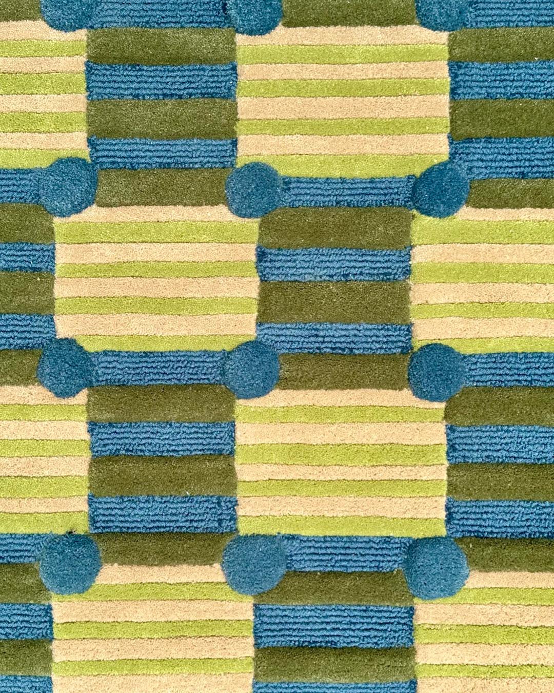 Bubble Grid is a bold experiment in structure and play. The rug features an interlocking pattern of ladder like forms in sea foam blue and olive green, connected by soft circular dots that add a playful rhythm to the composition. The base is a