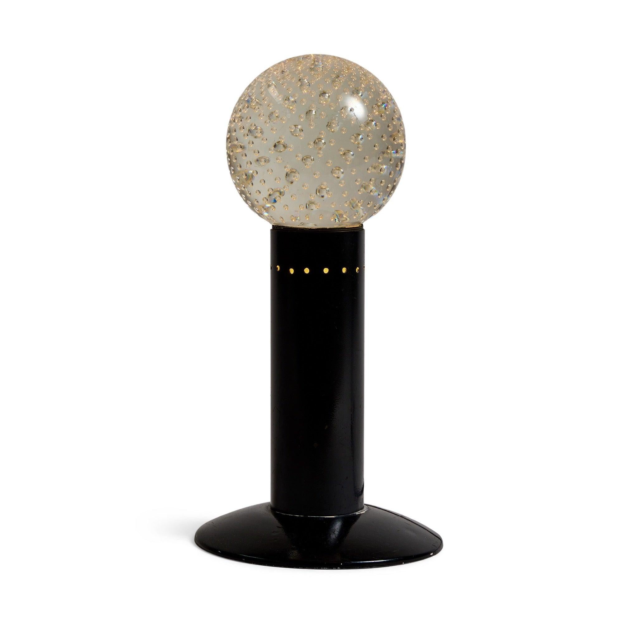 A table lamp with a round precision-bubble solid glass â€˜shade' that sits atop a black painted metal stem and base.